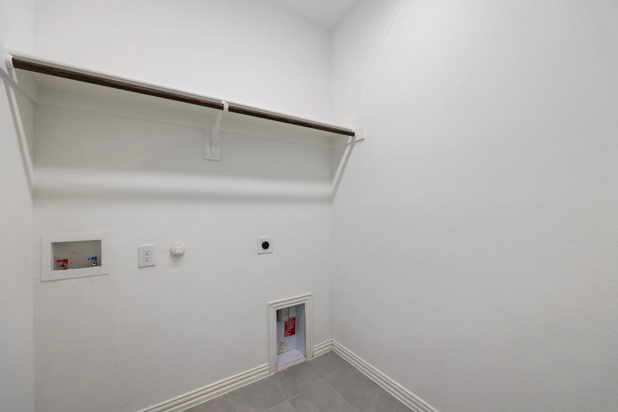 Laundry area with a hanging rod, tile flooring, and white walls