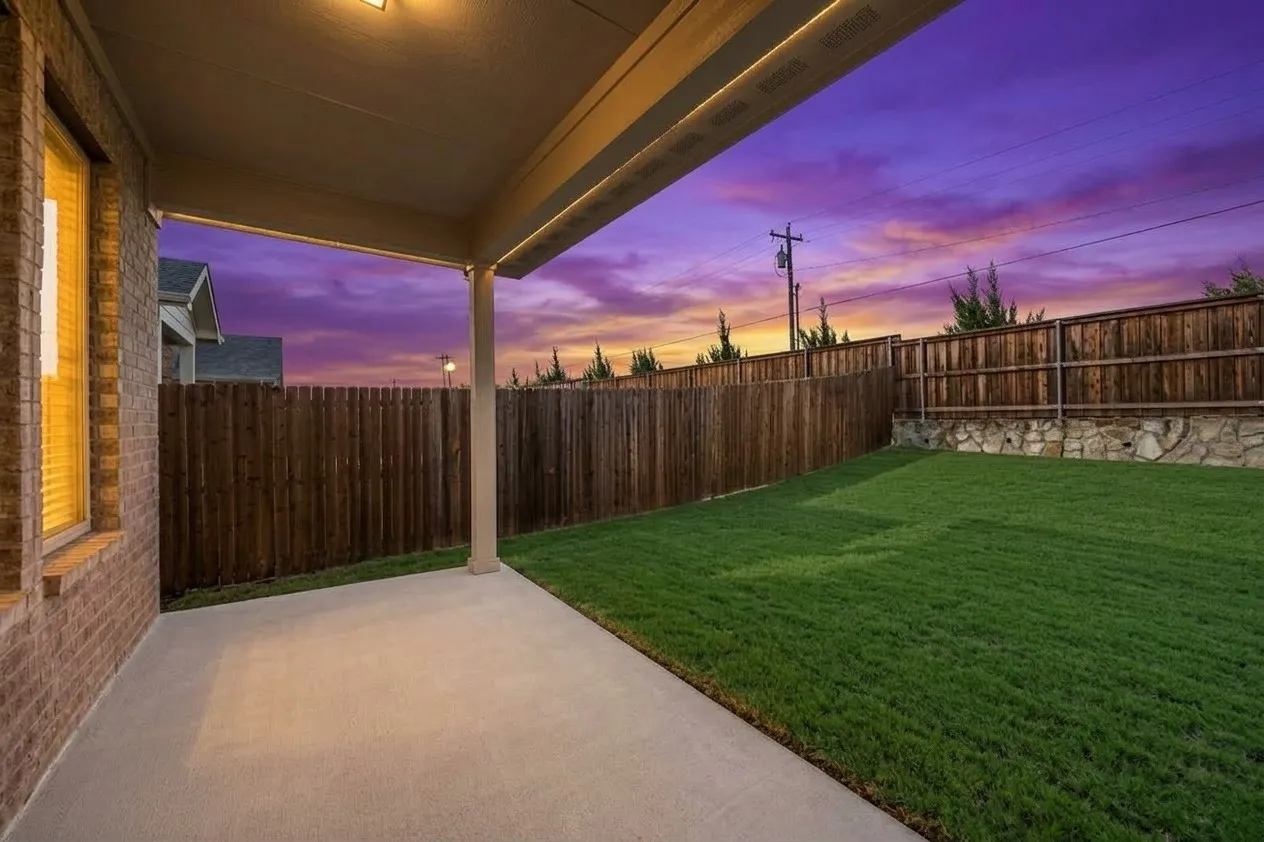 Covered concrete patio, expansive lawn, wood privacy fencing, and stone retaining wall