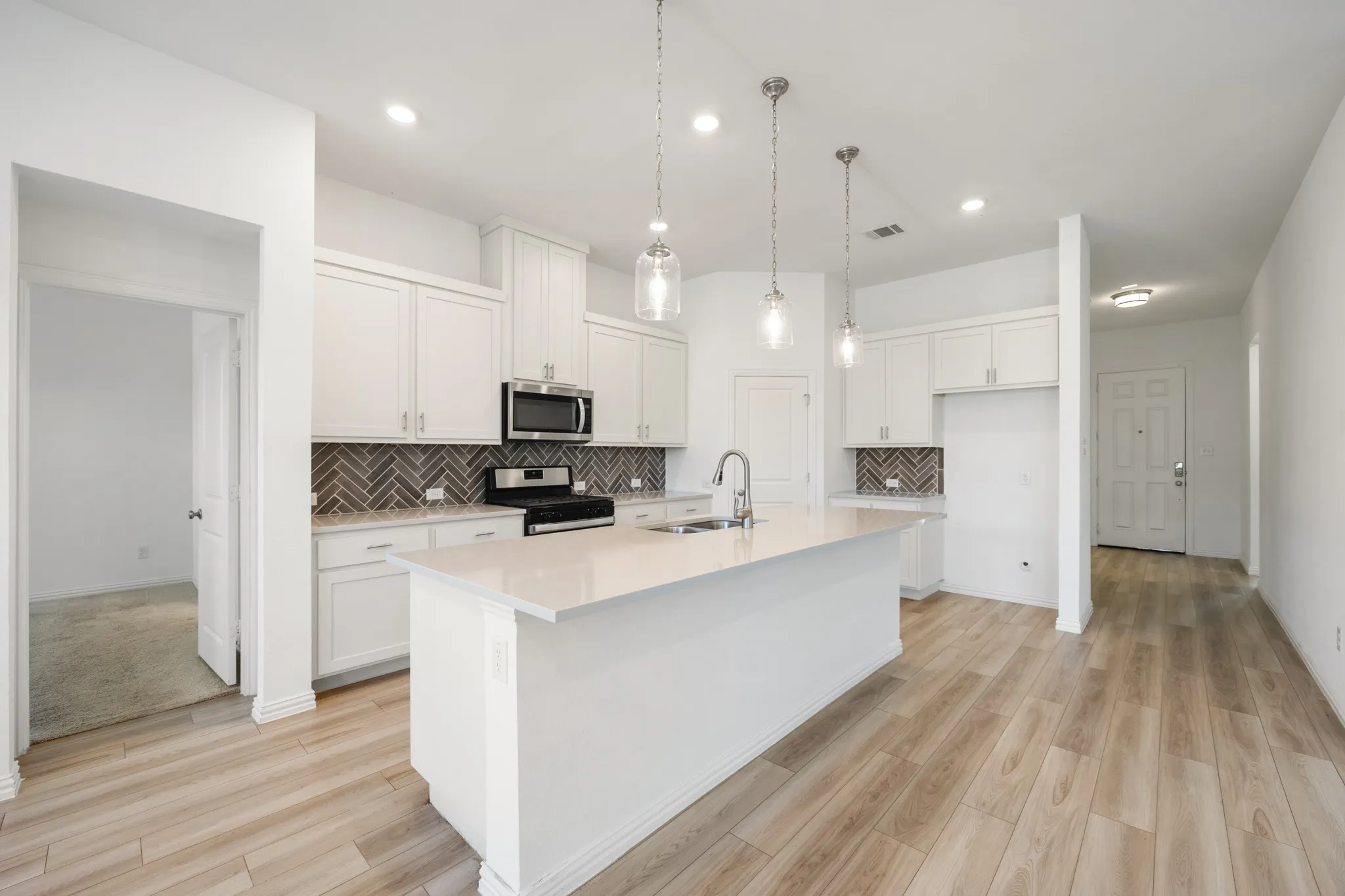 White cabinetry with brushed nickel hardware, herringbone pattern tile backsplash, stainless steel appliances, central island with undermount sink, and wood-finish flooring