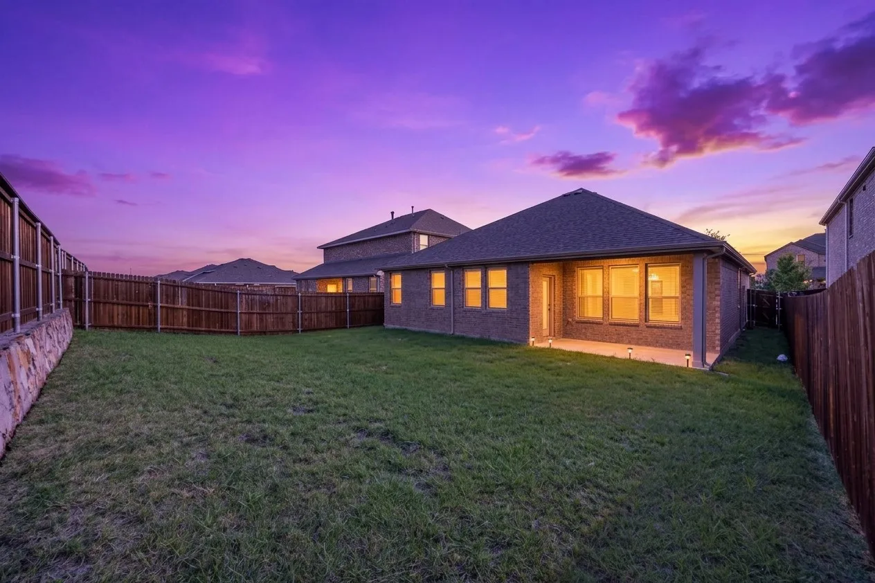Expansive backyard featuring a manicured lawn, full perimeter fencing, and a stone retaining wall