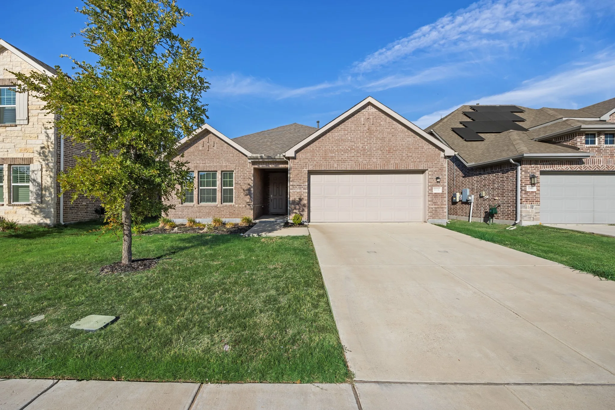 Brick exterior with an attached garage, concrete driveway, and established front landscaping