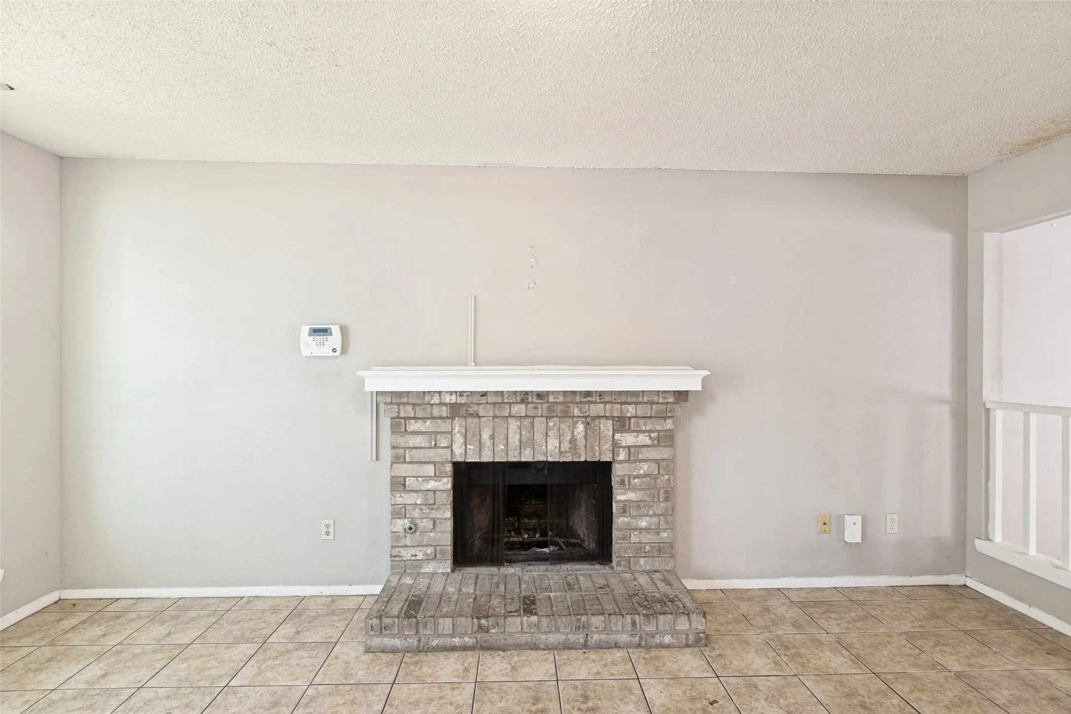 Brick fireplace with a white mantel, tile flooring, and light-colored wall paint