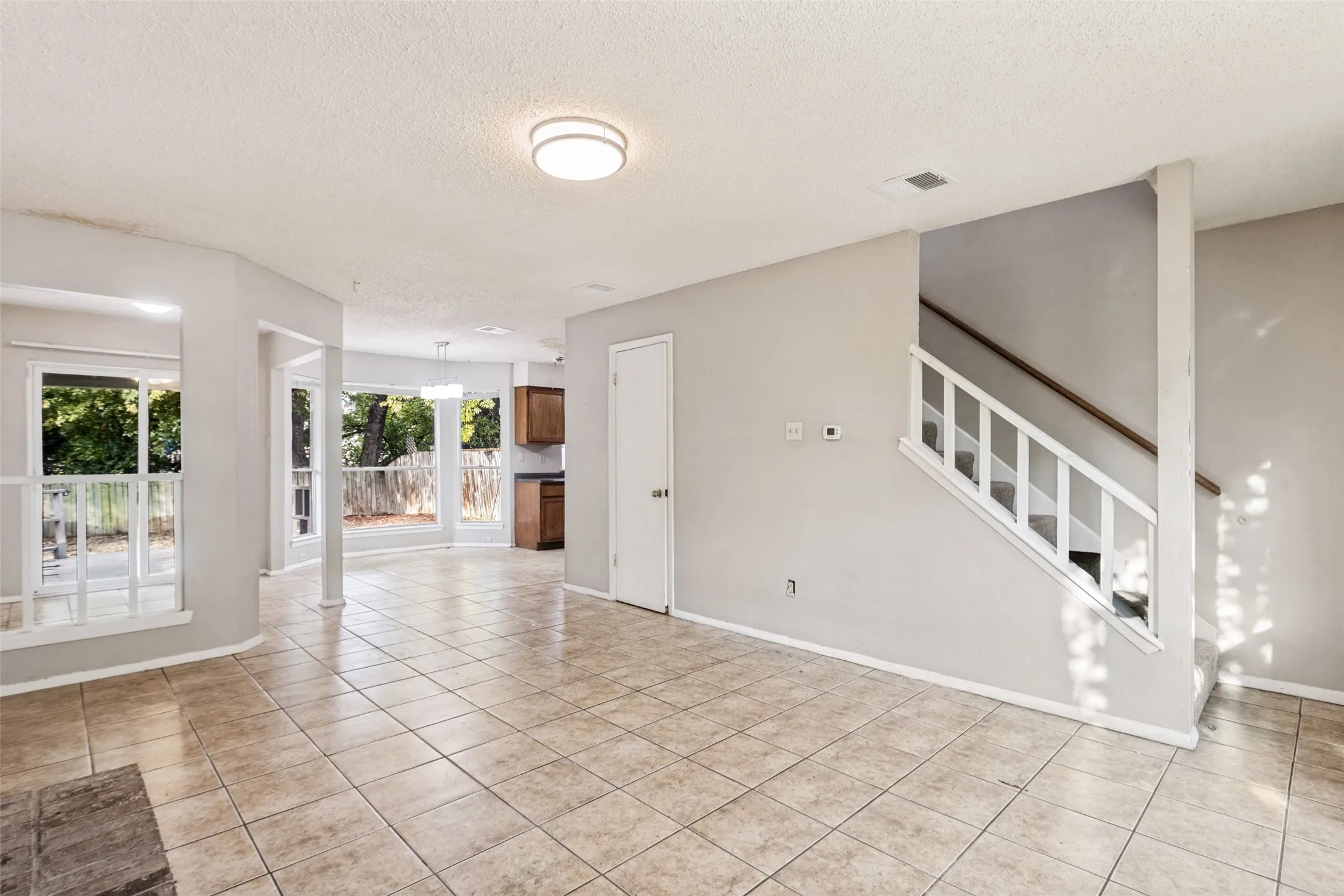 Expansive tiled flooring throughout, staircase with wood handrail, multiple large windows, and recessed lighting