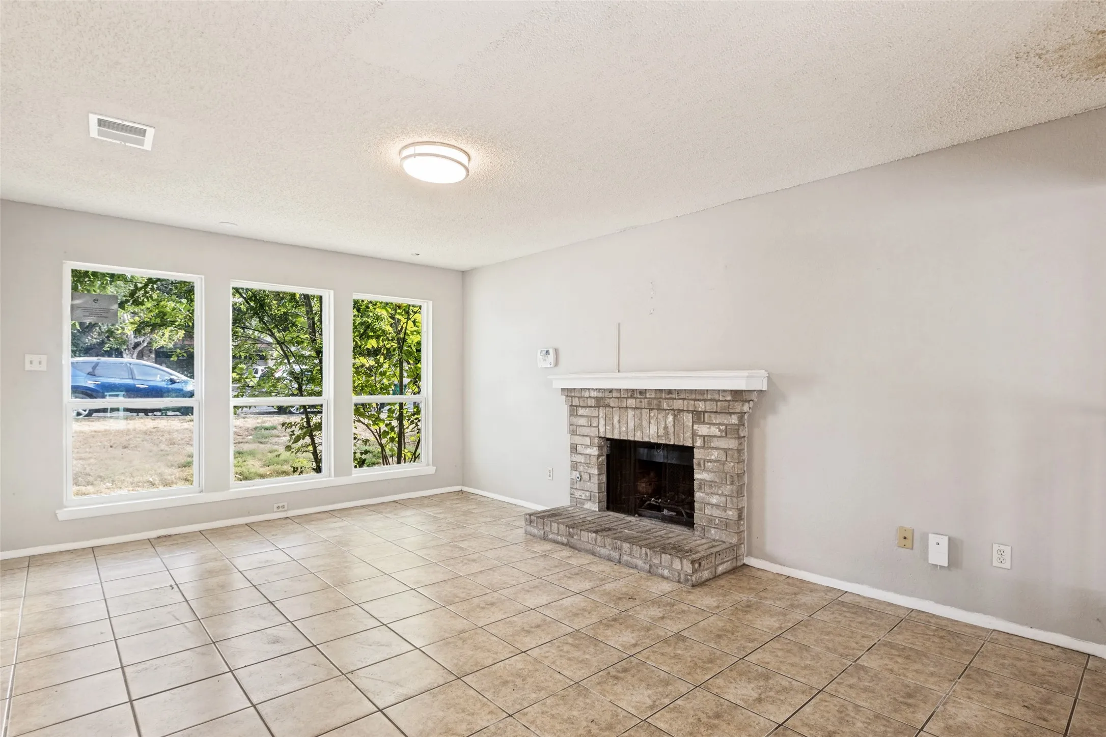 Tile flooring, three large windows, brick fireplace with mantel, and flush-mount ceiling light fixture