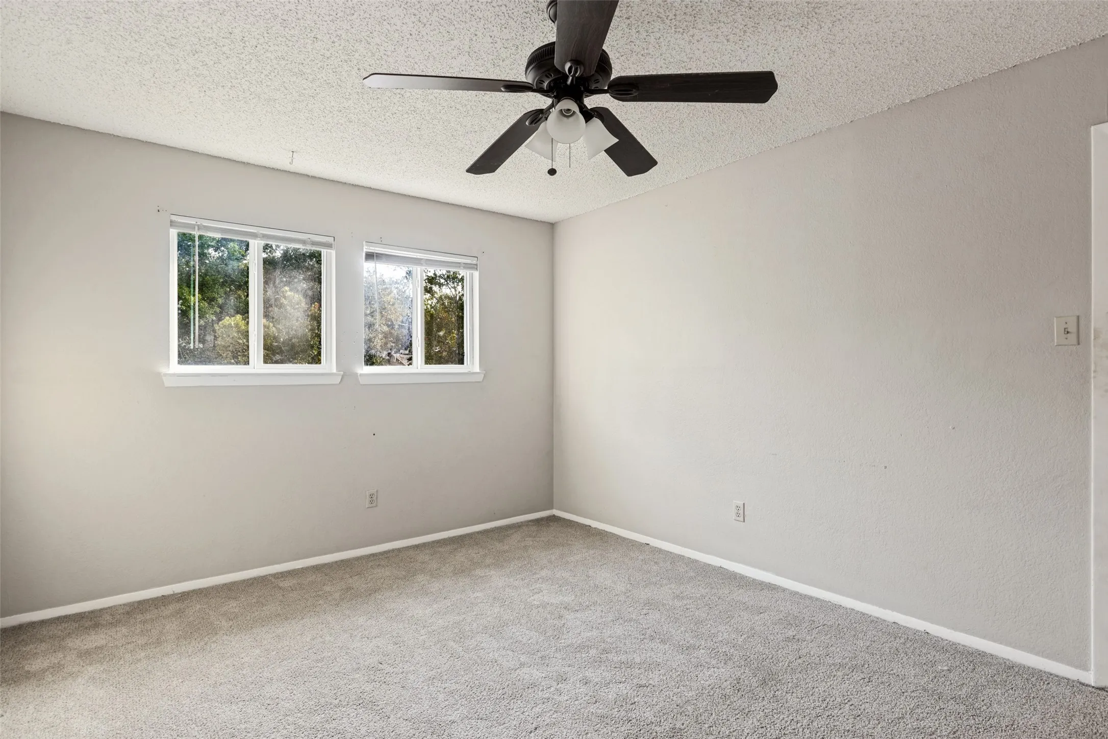 Recessed windows with blinds, ceiling fan with integrated lighting, neutral wall paint, and gray carpeting