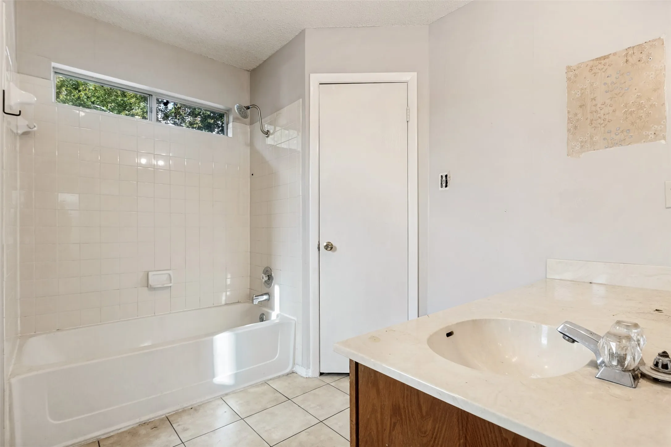 Bathroom featuring a white bathtub with subway tile surround, tiled flooring, wood-finish vanity with an integrated sink, and an upper transom window
