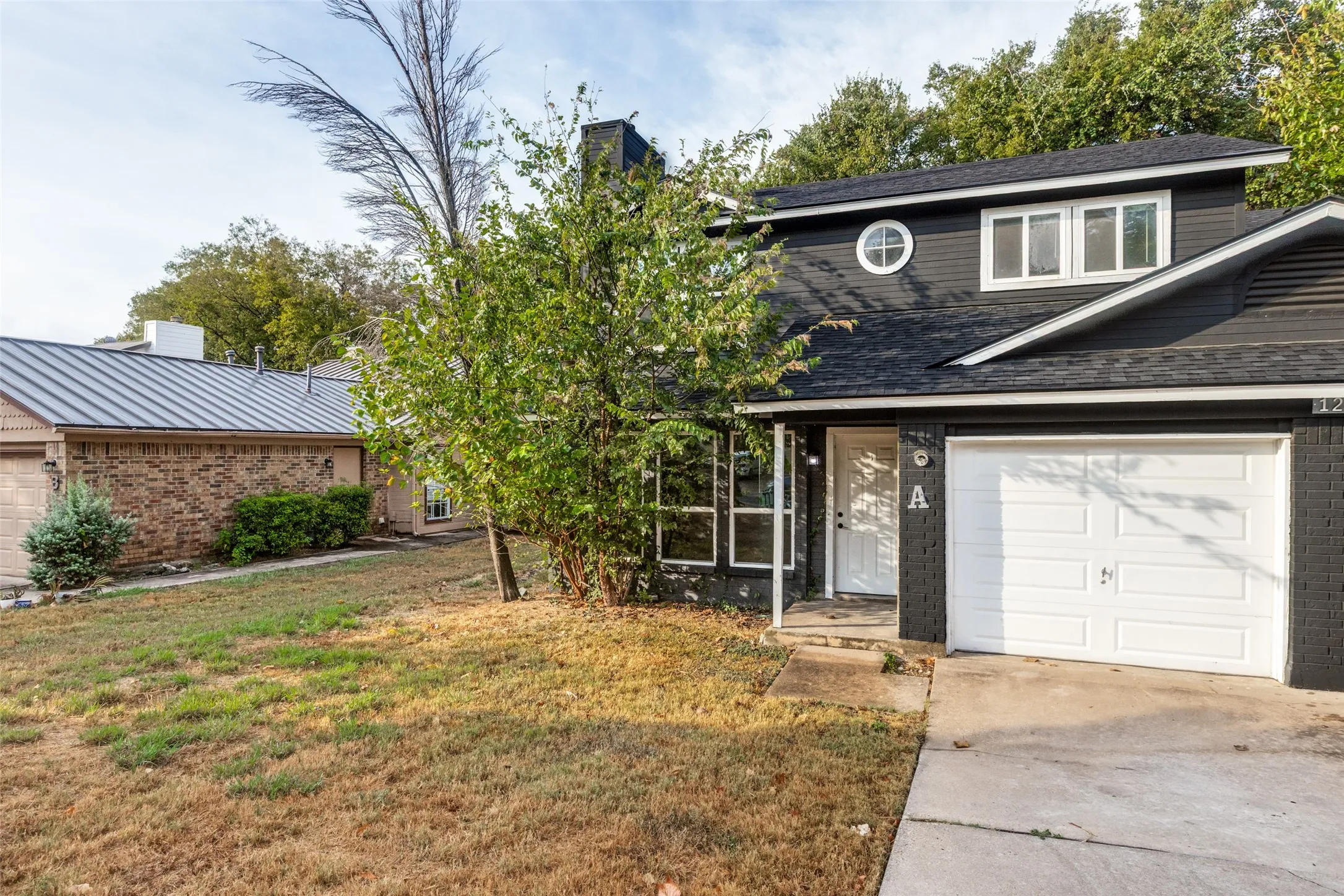 Two-story exterior with dark siding and brick accents, featuring a white garage door and a round window on the upper level