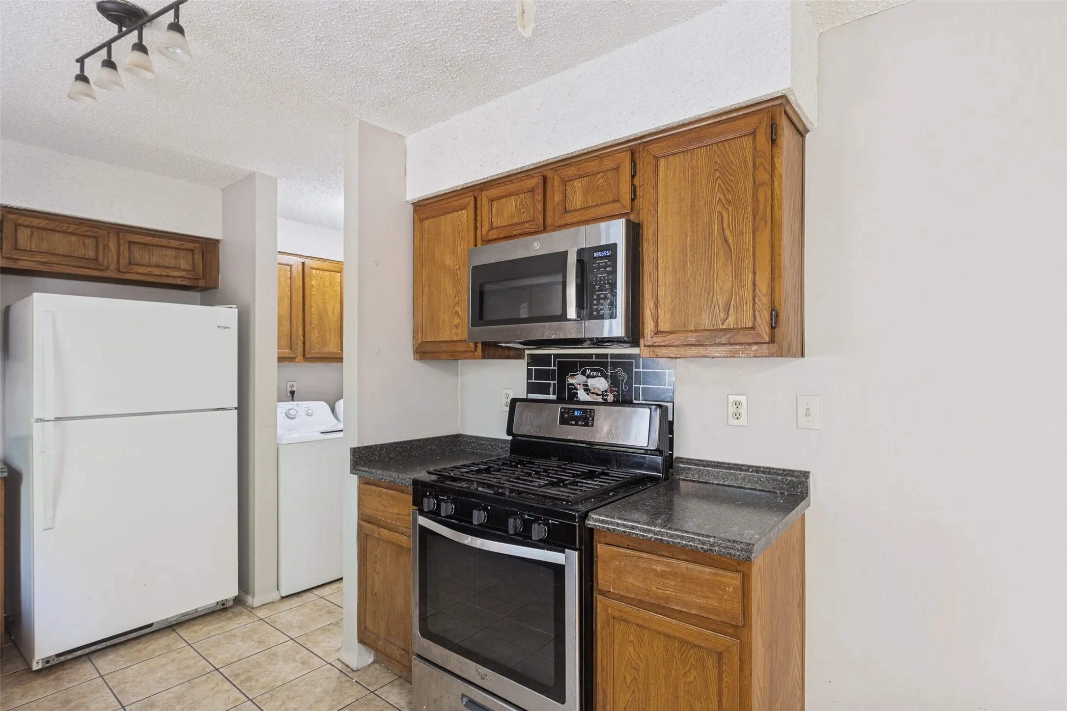 Efficient kitchen featuring wood-finish cabinetry, stainless steel gas range with black finish, built-in microwave, and dark countertops