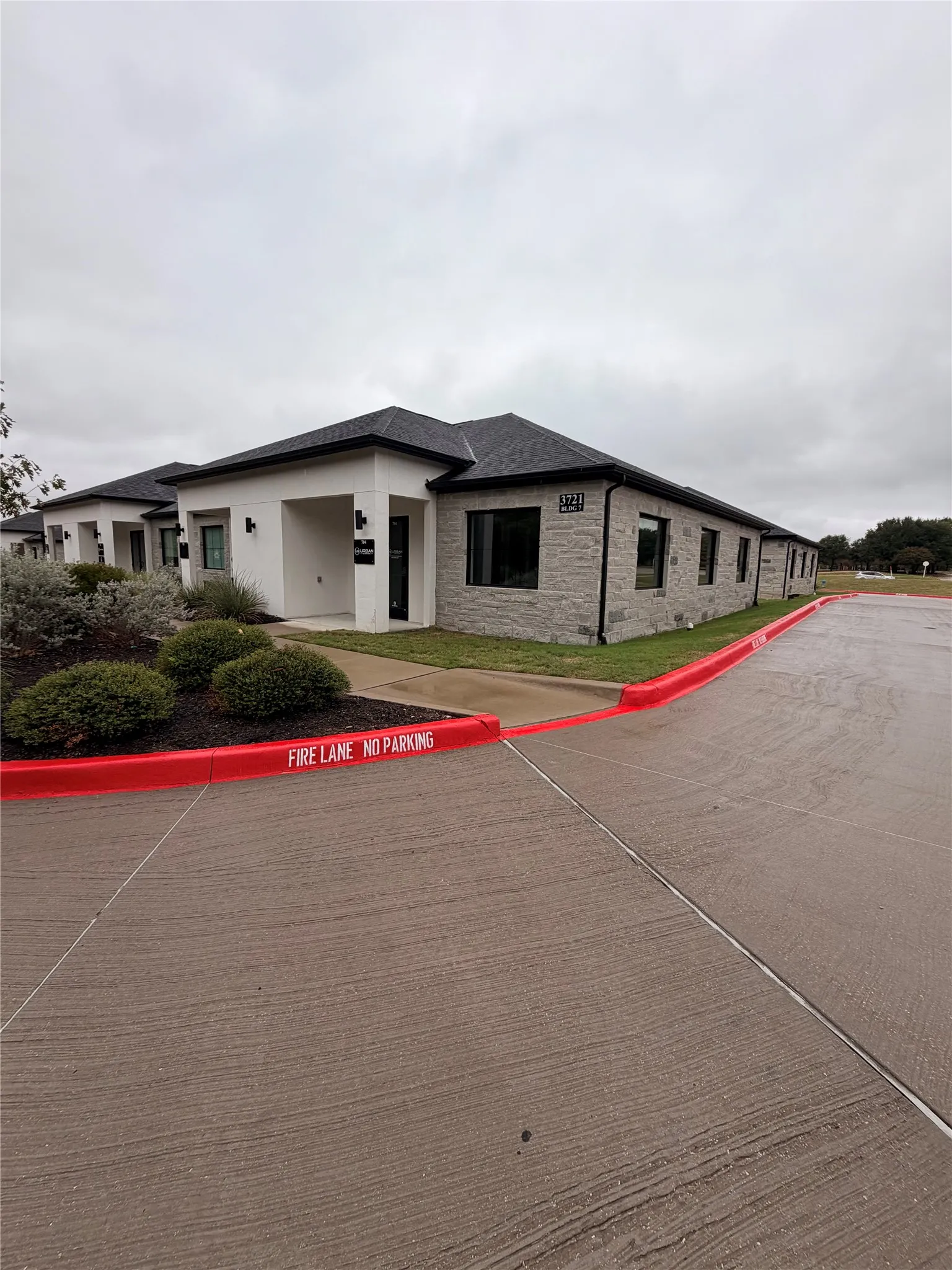 Building exterior featuring a black shingle roof, stone veneer, white stucco facade, and dark framed windows