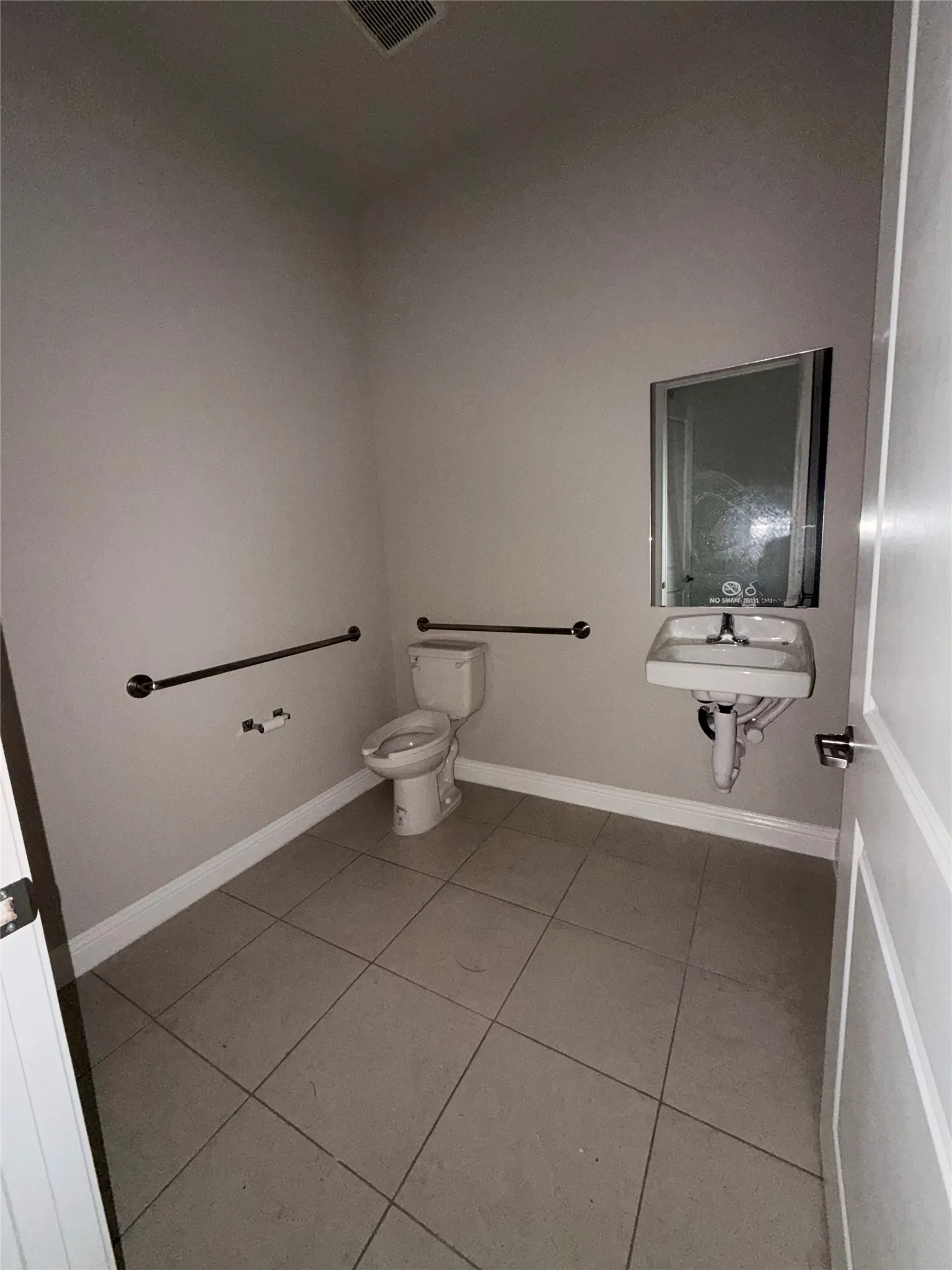 Tiled flooring, wall-mounted sink, toilet, built-in grab bars, and a white paneled door