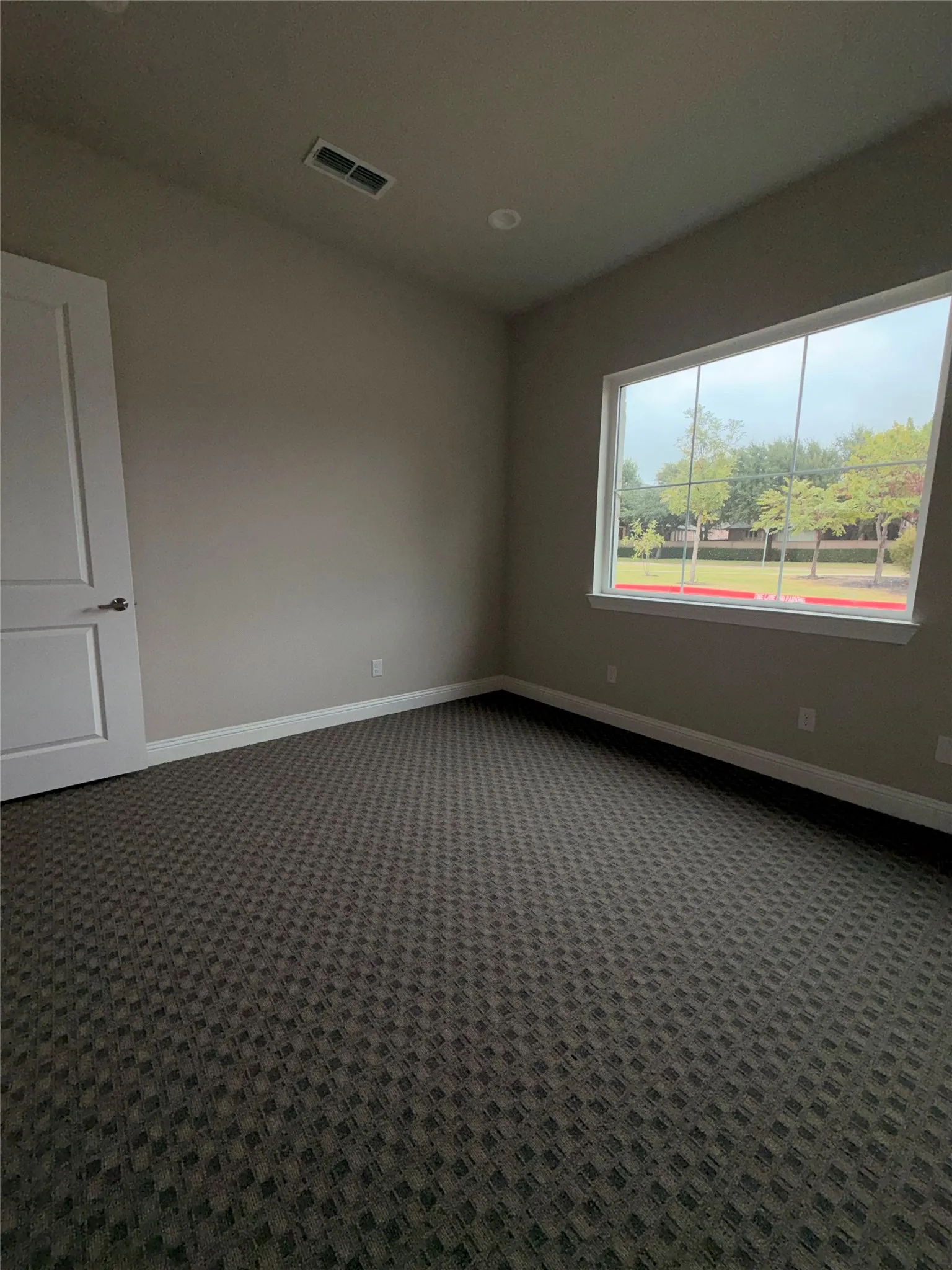 Neutral tone wall paint, patterned carpet flooring, recessed ceiling lighting, and a window with white trim