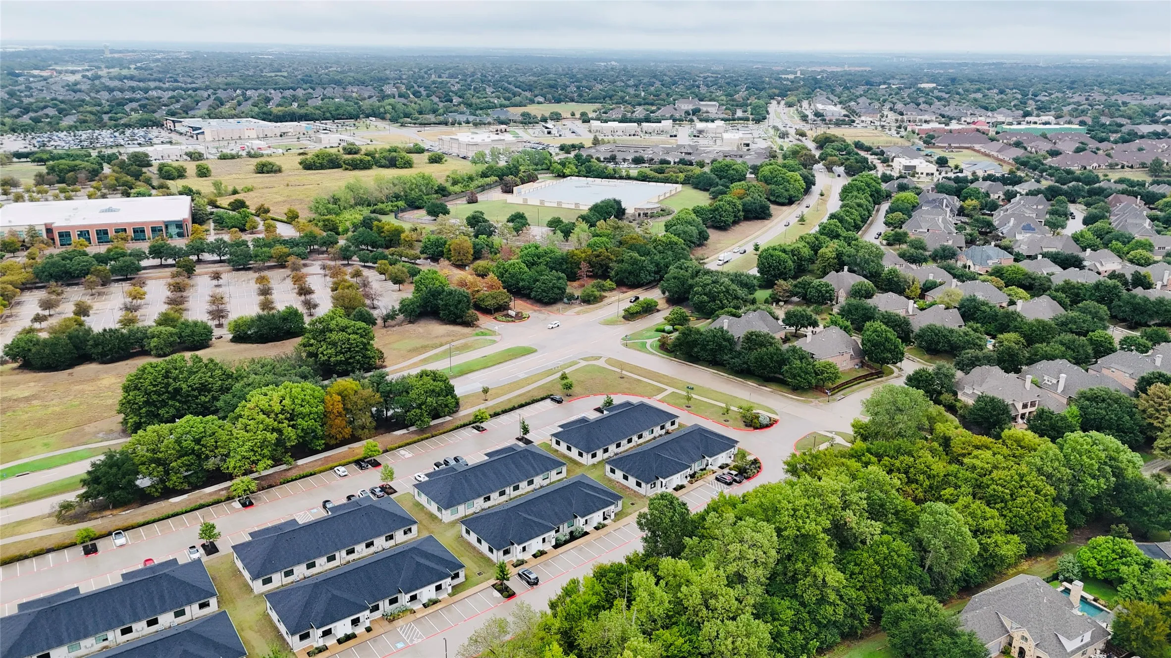 Aerial perspective showcasing commercial properties with dark roofs, surrounded by lush mature trees, and a residential area with varied rooflines
