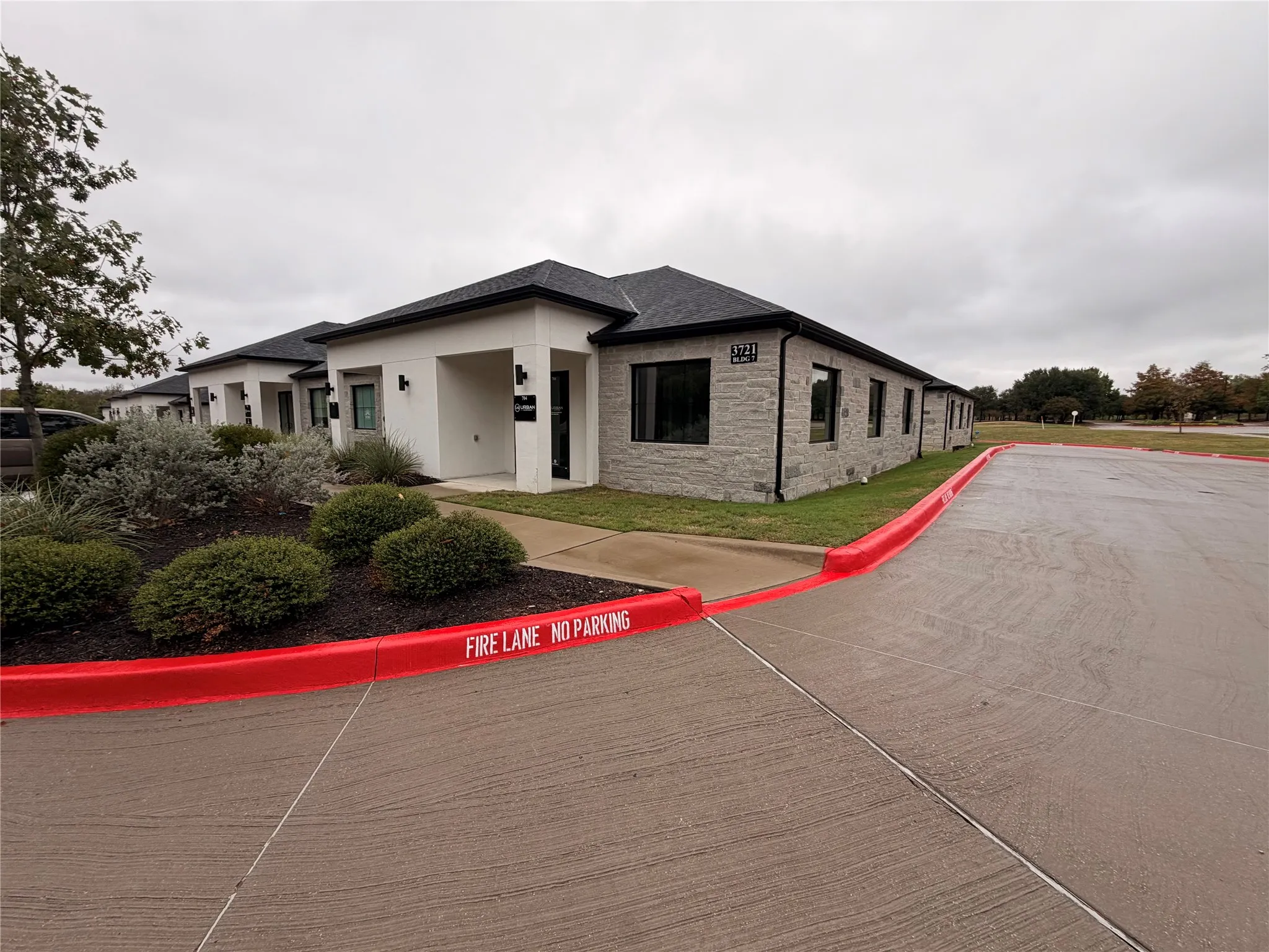Modern stucco and stone-clad exterior with dark-framed windows, a dark shingle roof, and established landscaping