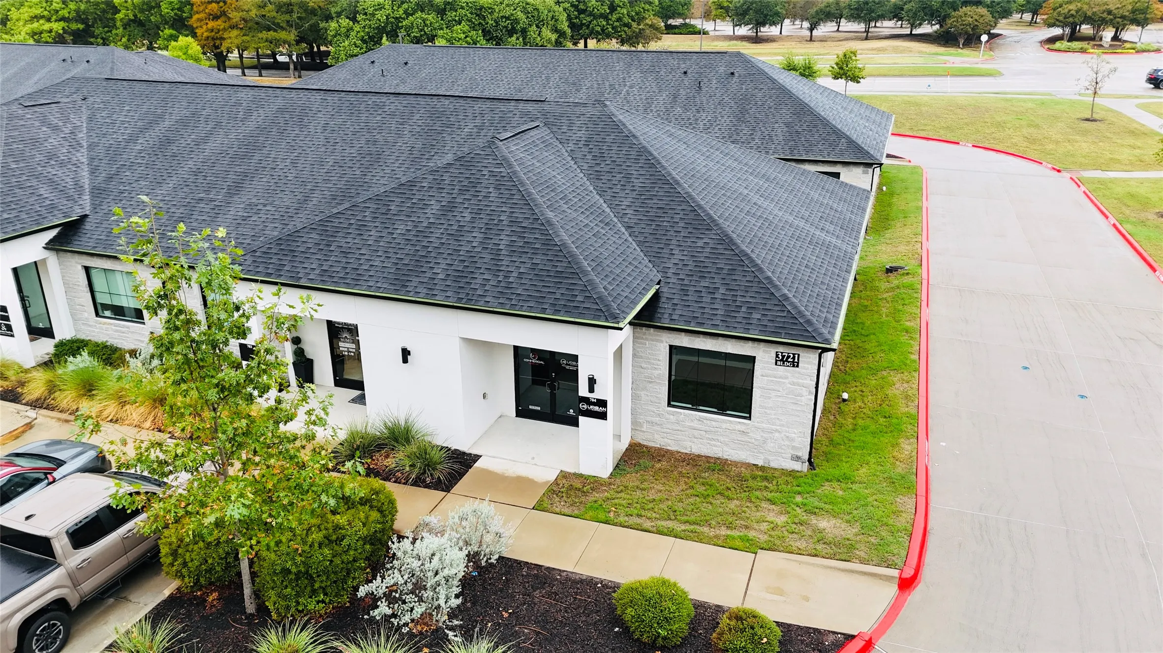 Modern commercial building featuring a dark shingle roof, white exterior with stone accents, and manicured landscaping