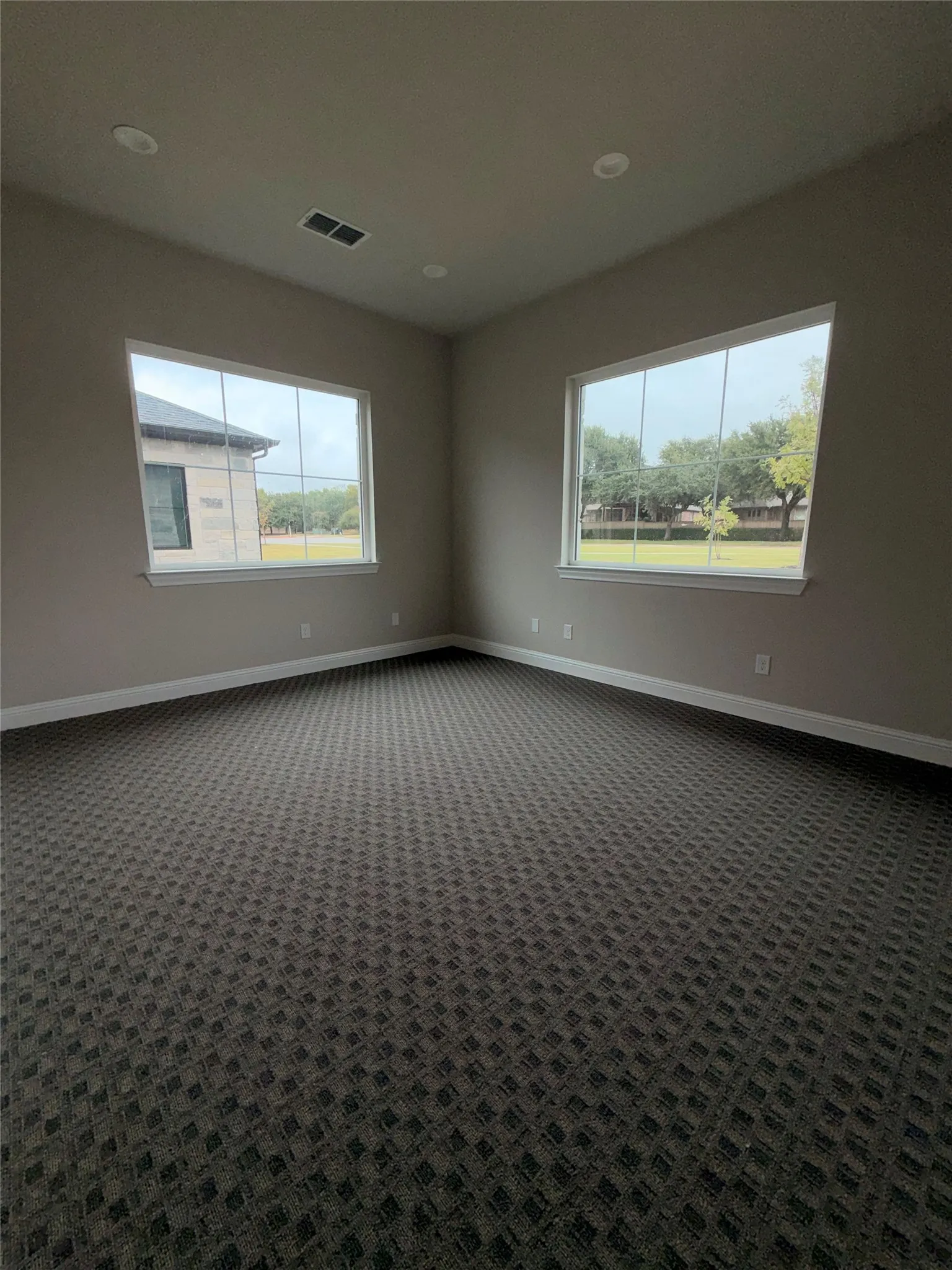 Recessed lighting, patterned carpet flooring, and two large windows with white trim