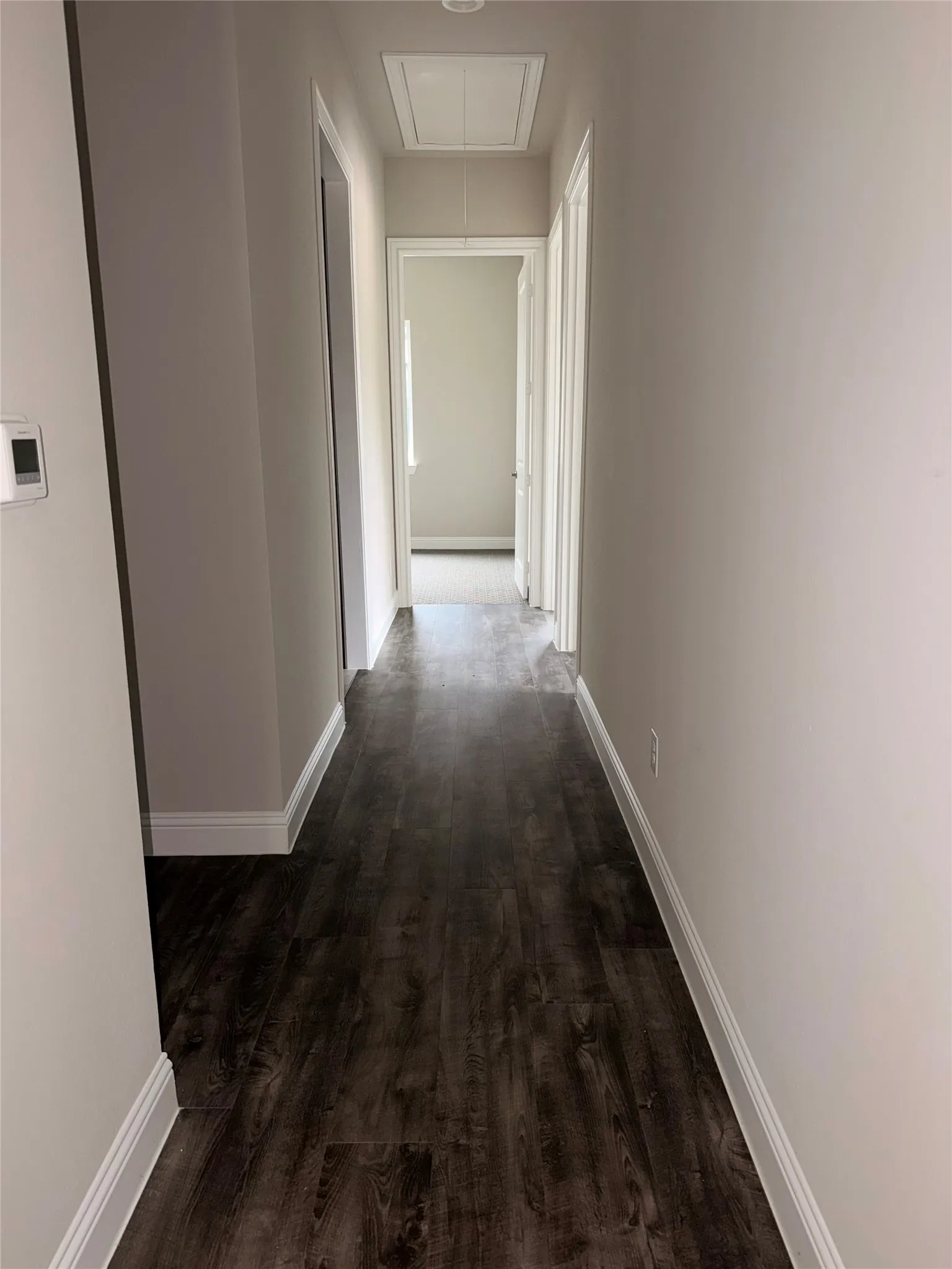 Hallway featuring dark wood-finish flooring, light neutral wall paint, white trim, and a recessed ceiling light