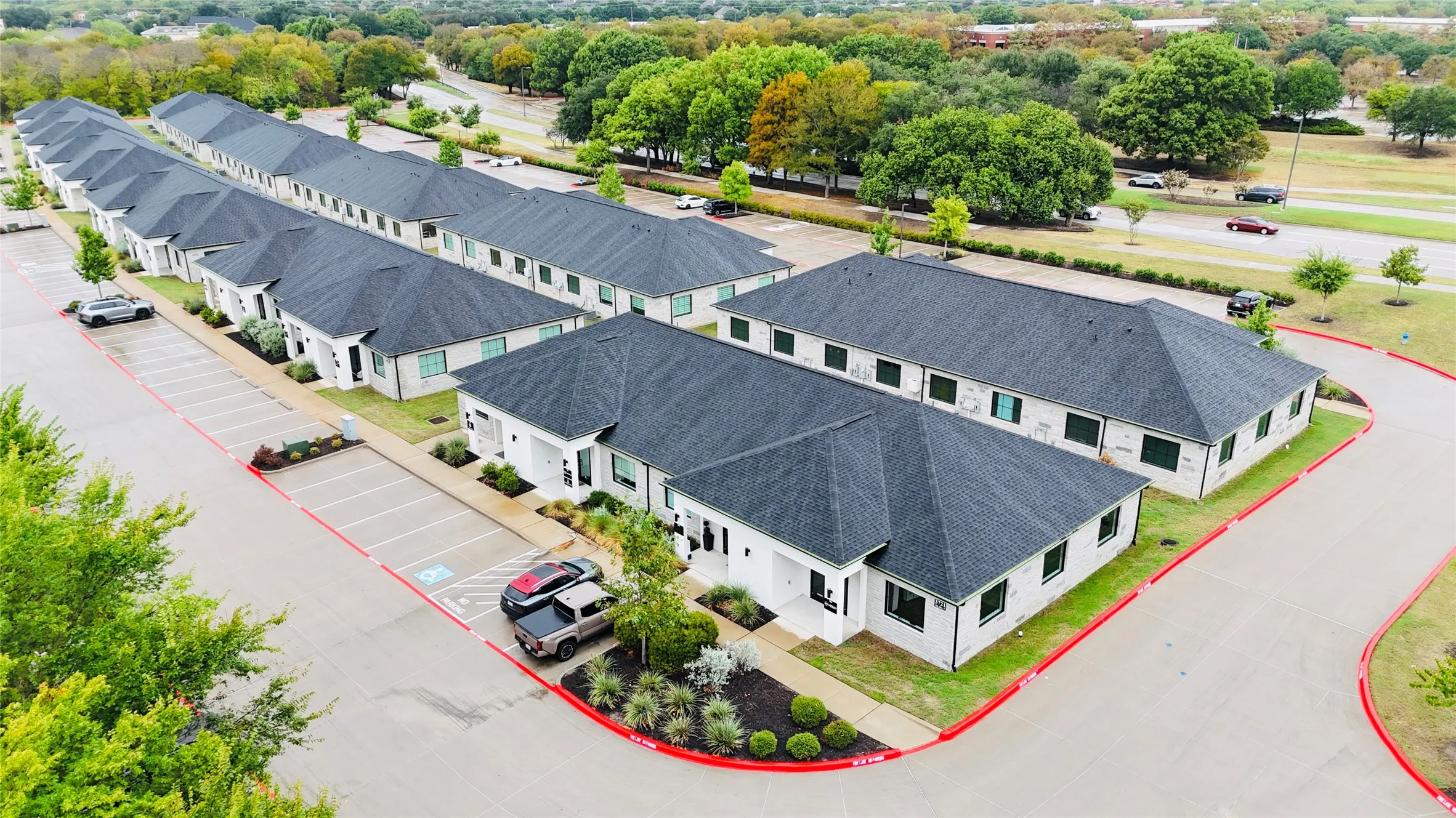 Multiple single-story structures with dark shingle roofs, white exteriors, and green landscaping