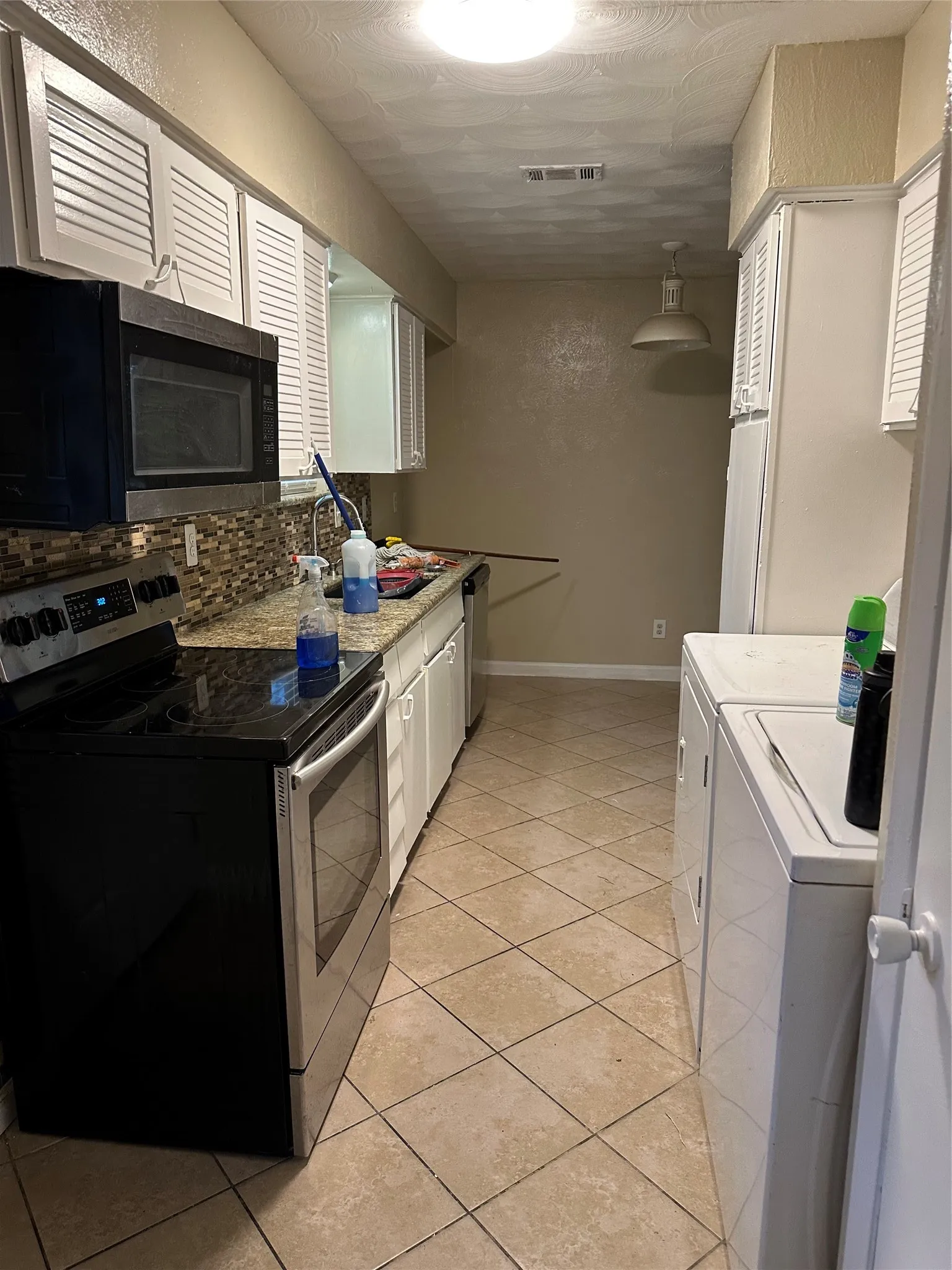Kitchen featuring white louvered cabinetry, tiled backsplash, and light-toned tile flooring