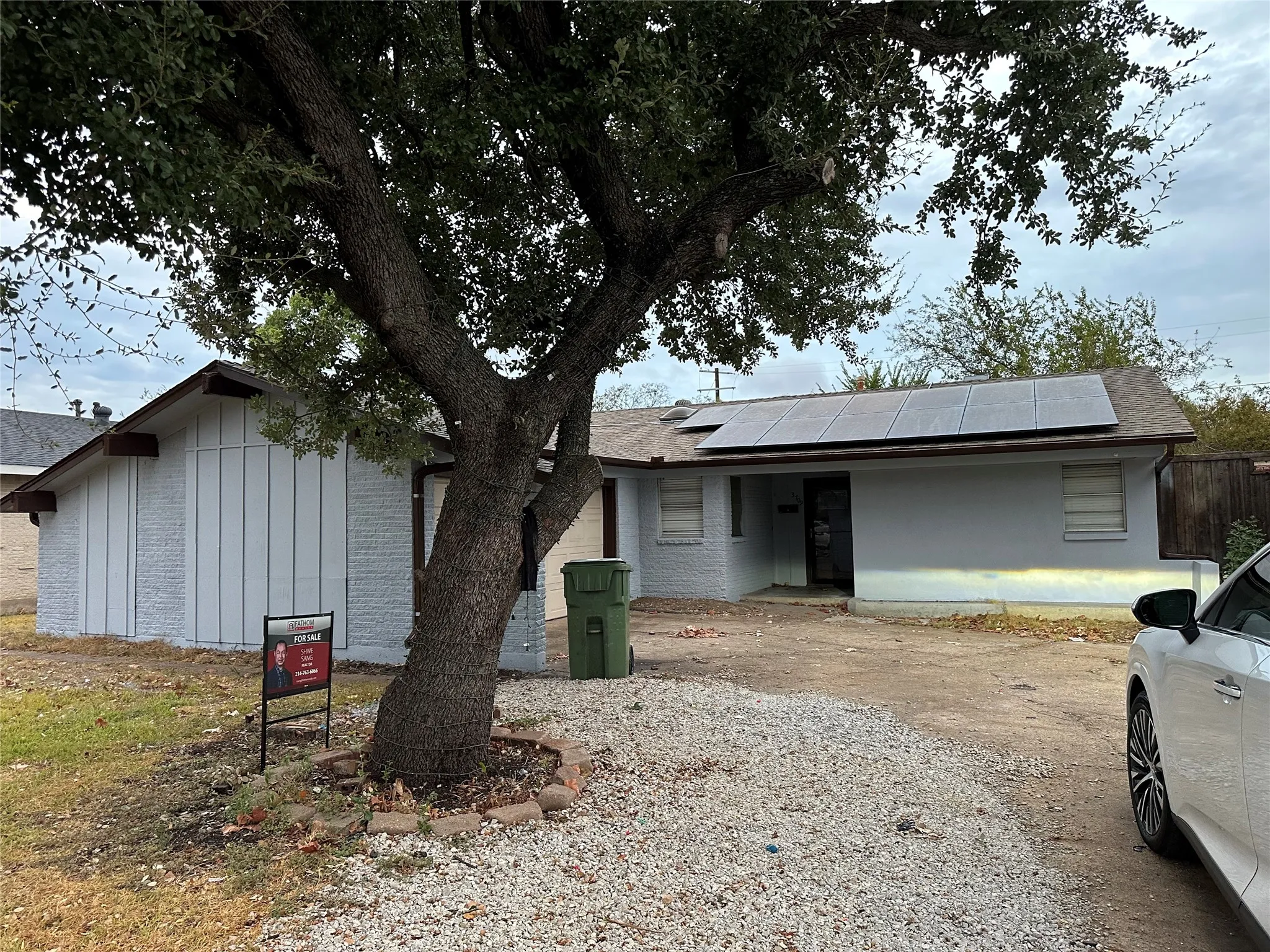 Single-story residence featuring a gray exterior, a gravel driveway, and solar panels on the roof