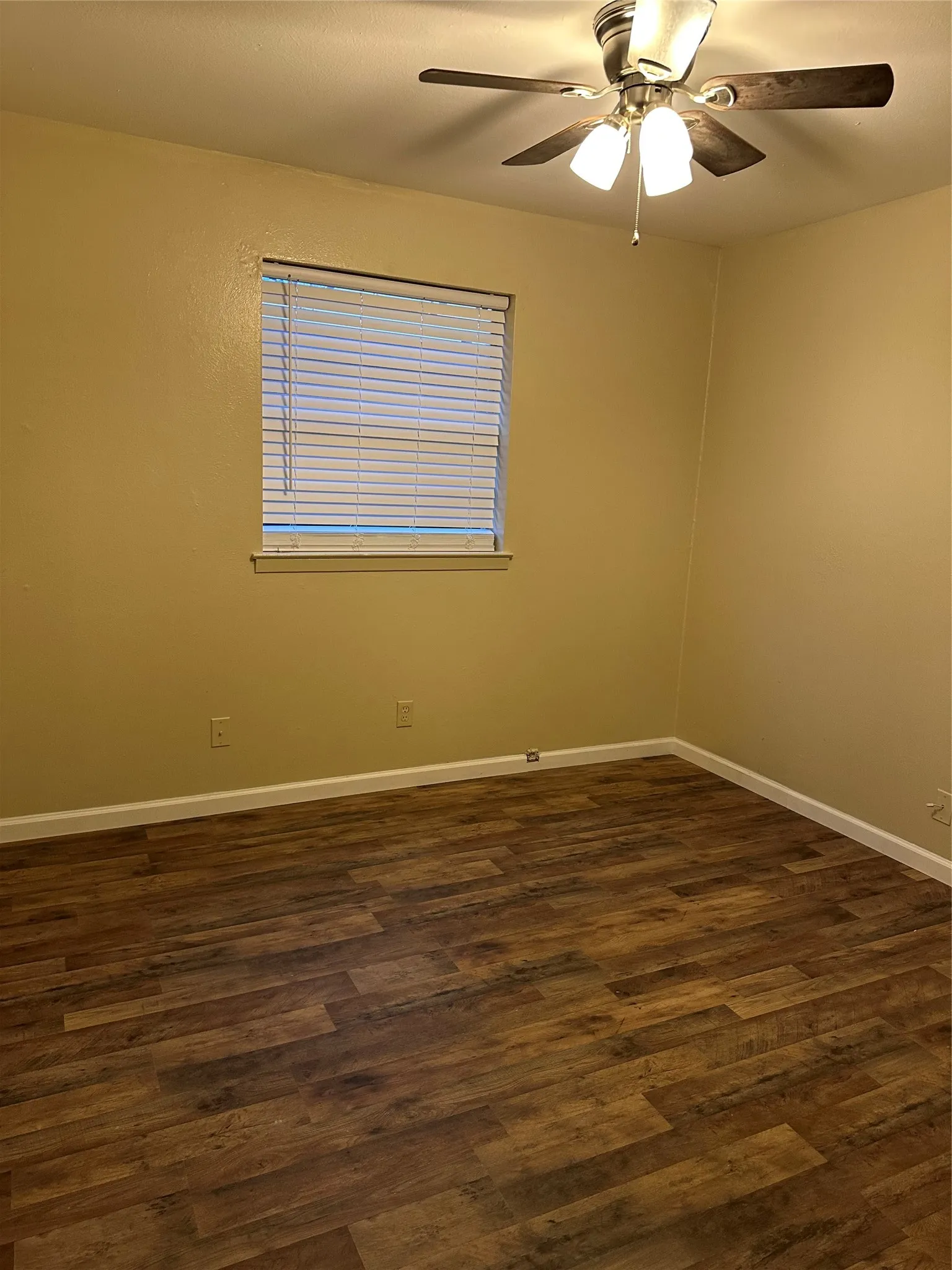 Wood-finish flooring throughout, window with blinds, and ceiling fan with integrated lighting