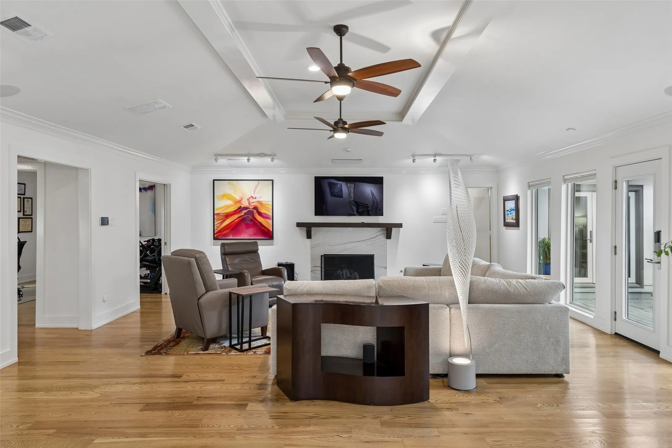Spacious Living at the Heart of the Home — This generously sized living area offers expansive hardwood flooring, a raised ceiling treatment, multiple seating zones, and direct access to the outdoor living spaces.
