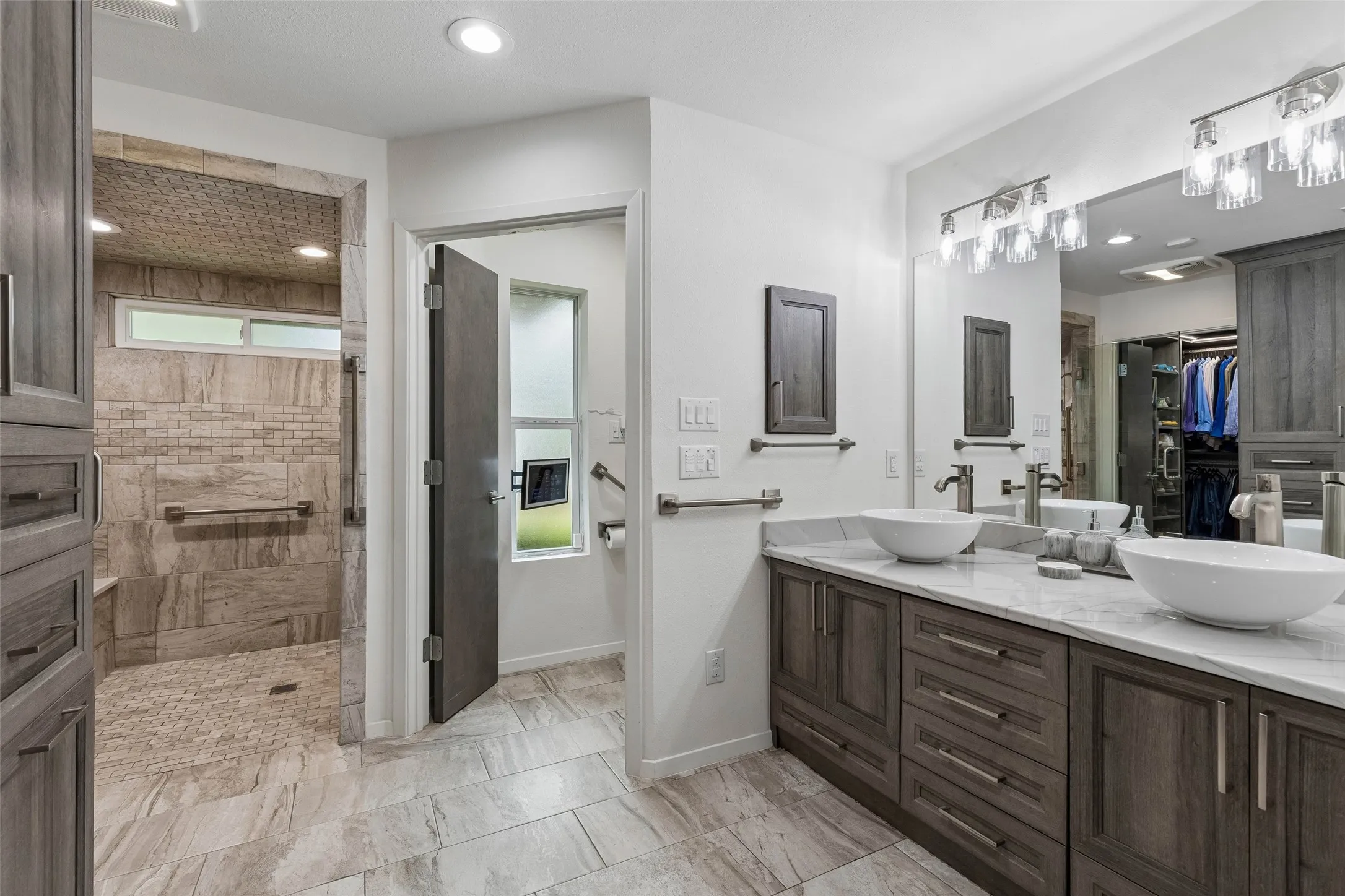 Remodeled Primary Bath with Thoughtful Storage — Dual vessel sinks, extensive cabinetry, updated lighting, and a spacious layout create a highly functional bath designed for everyday comfort.