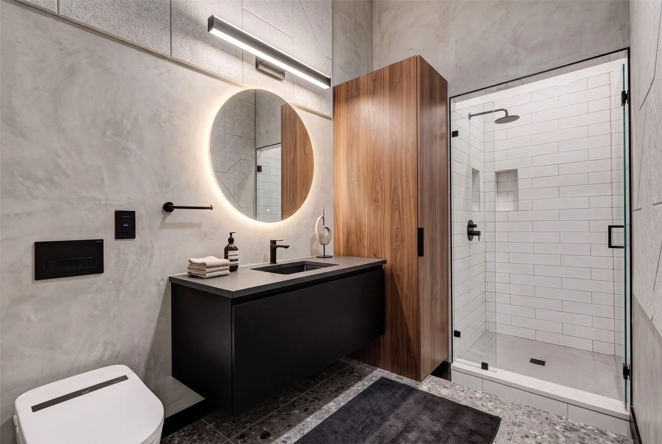 Floating vanity with a rectangular sink, a large backlit circular mirror, a glass-enclosed shower with subway tile, built-in recessed shelving, and a wood-finish storage cabinet - AI Generated