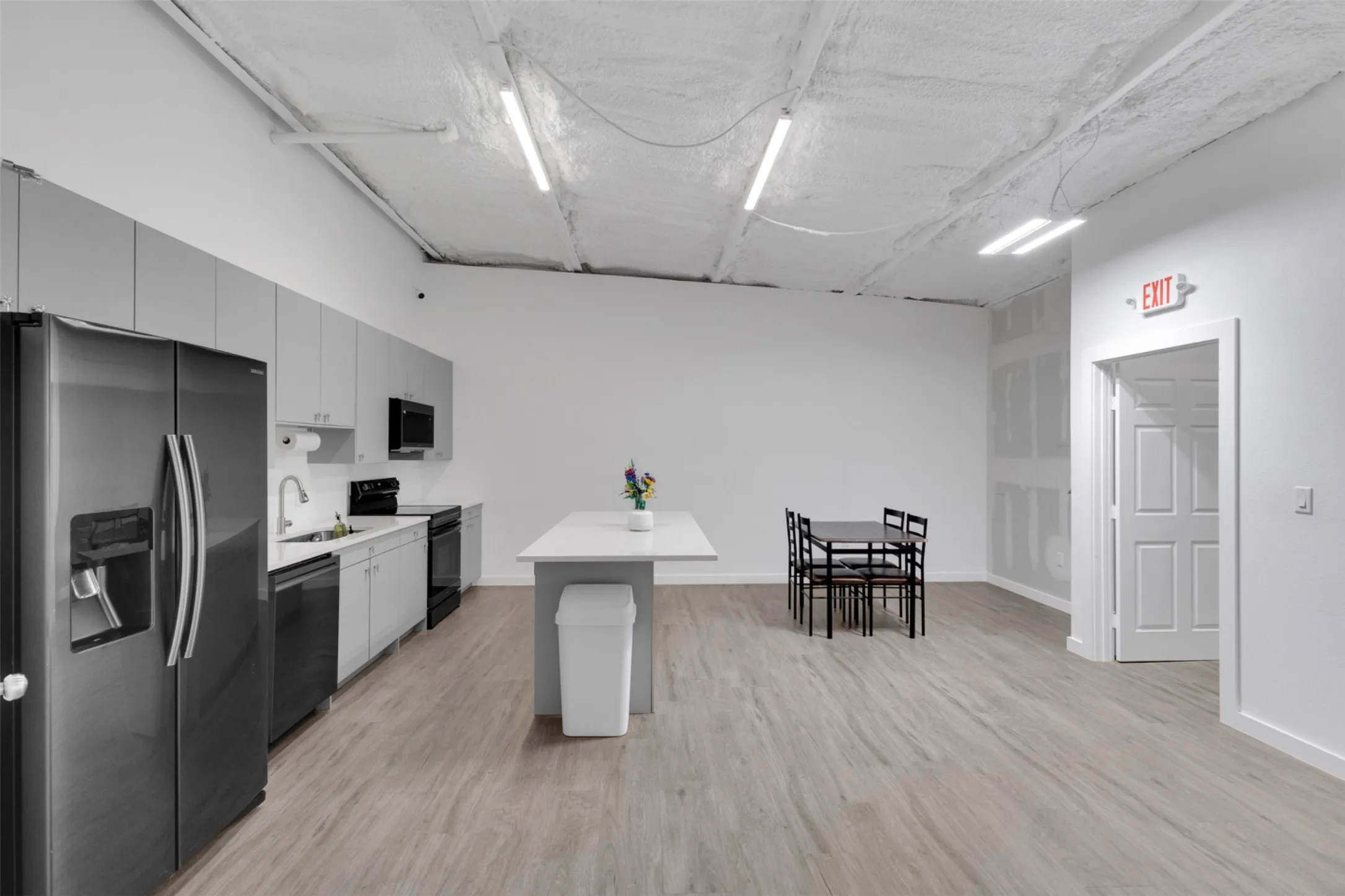 Galley kitchen with light gray cabinetry, stainless steel refrigerator, and wood-finish flooring