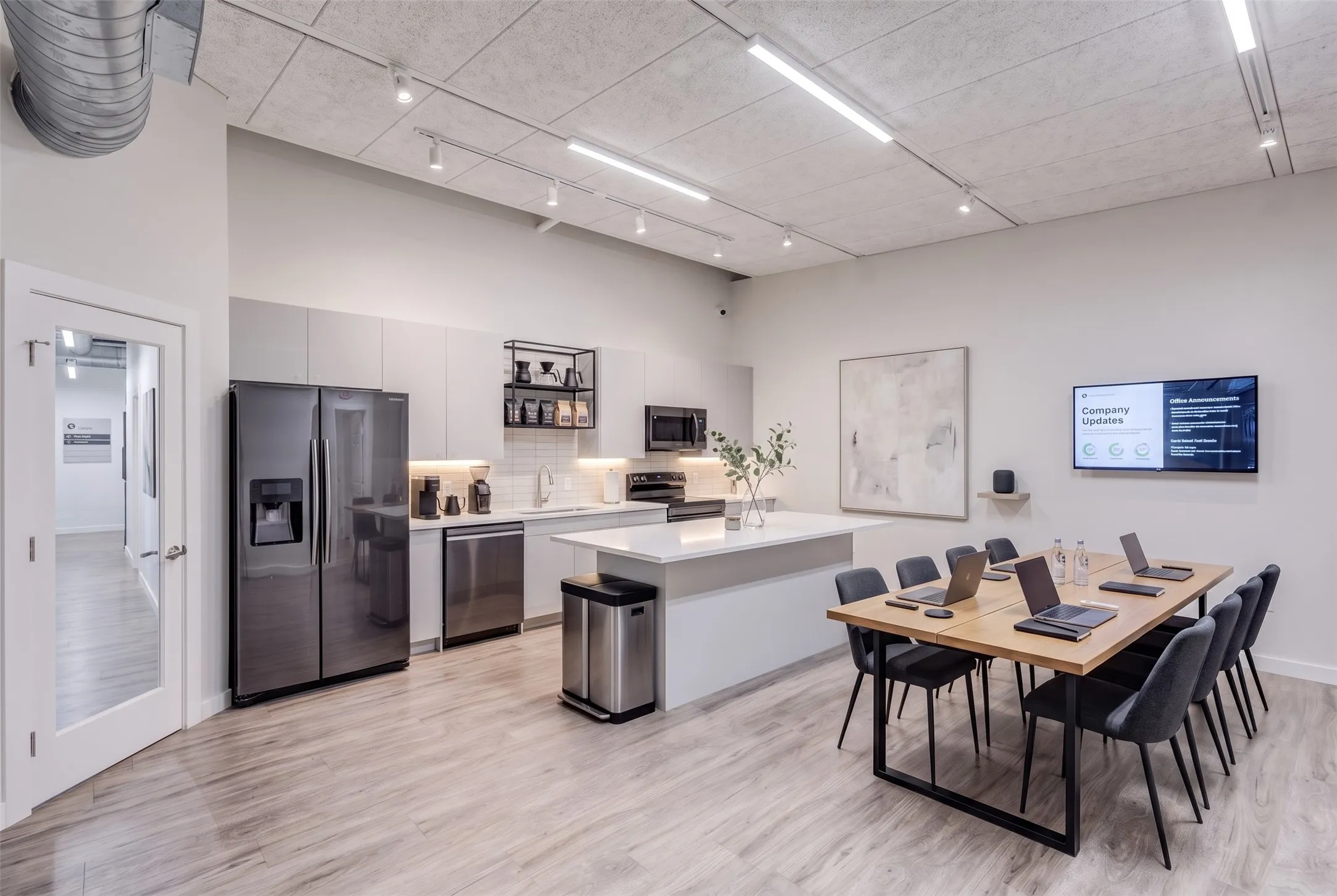 Contemporary kitchen area featuring stainless steel appliances, flat-panel cabinetry, a central island with a quartz-like countertop, wood-finish flooring, and exposed ductwork