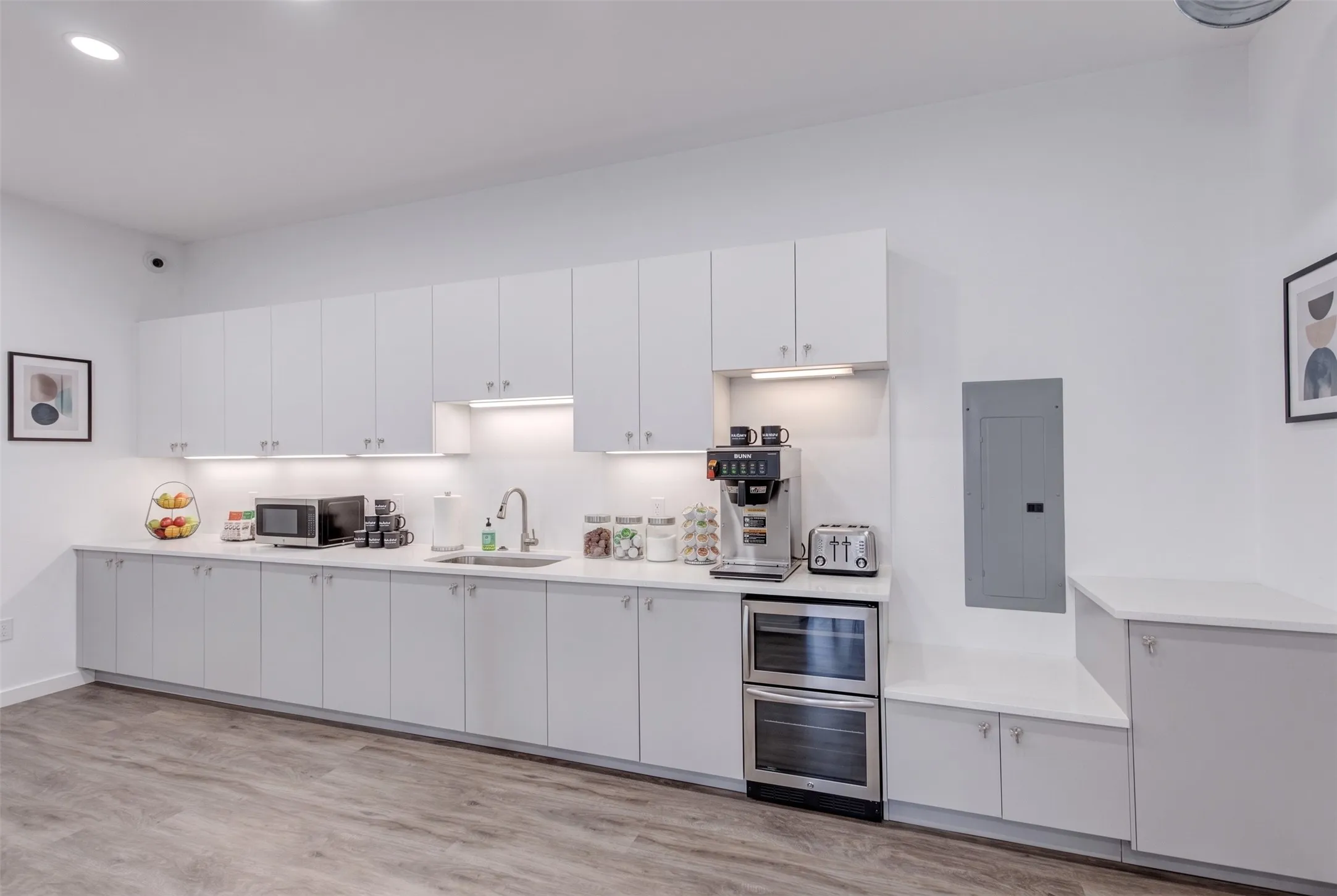 Extensive white cabinetry with under-cabinet lighting, stainless steel sink, wood-finish flooring, and integrated double ovens