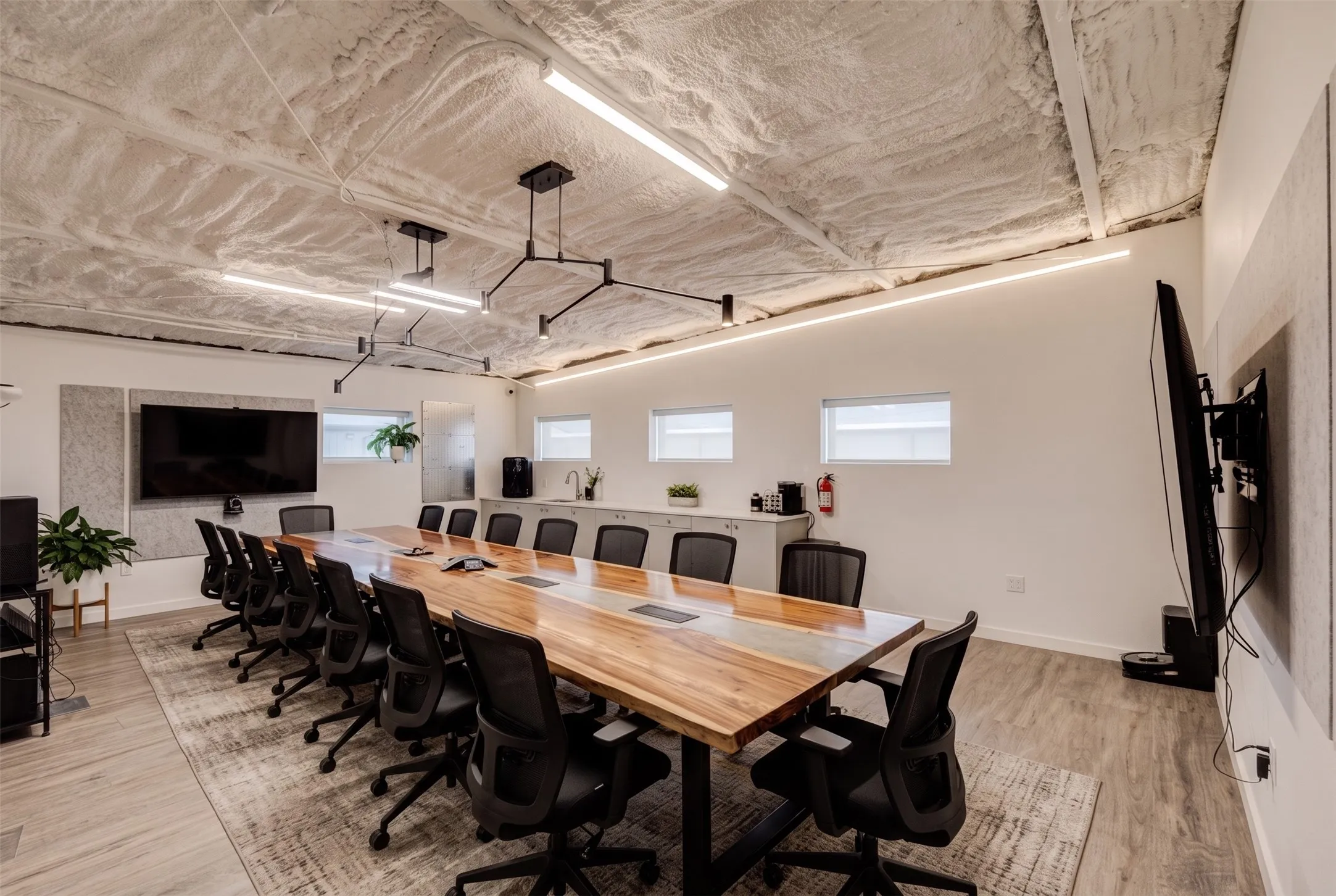 Expansive meeting room with a large wood-finish conference table, contemporary linear lighting fixtures, and light wood-finish flooring- AI Generated