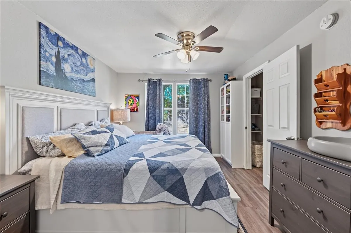 Wood-finish flooring, ceiling fan with integrated lighting, window with light-filtering curtains, and a built-in closet with double bifold doors