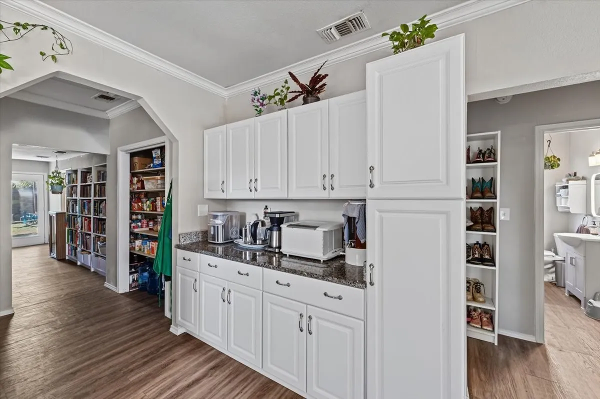 White cabinetry with brushed nickel hardware, granite-style countertops, wood-finish flooring, and pantry storage