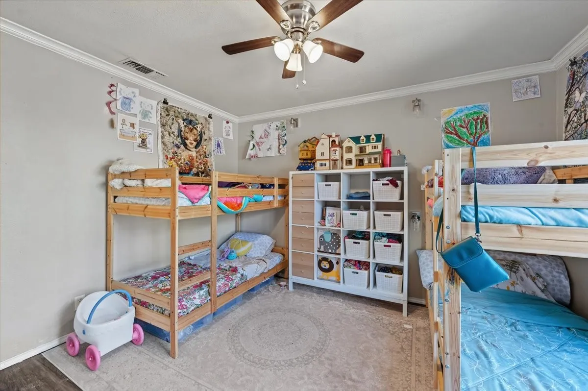 Neutral wall color, crown molding, wood-finish flooring, ceiling fan with integrated lighting, and a cubby storage unit