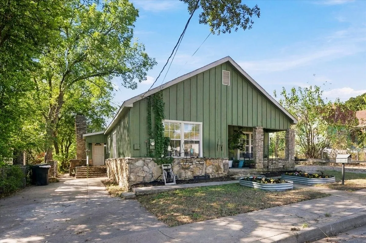 Gable-roof exterior with vertical siding, stone foundation, covered porch supported by stone columns, and a paved driveway