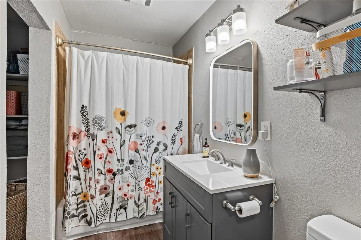 Bathroom featuring a single vanity with a white countertop and dark gray cabinetry, wall-mounted mirror, and a three-light vanity fixture
