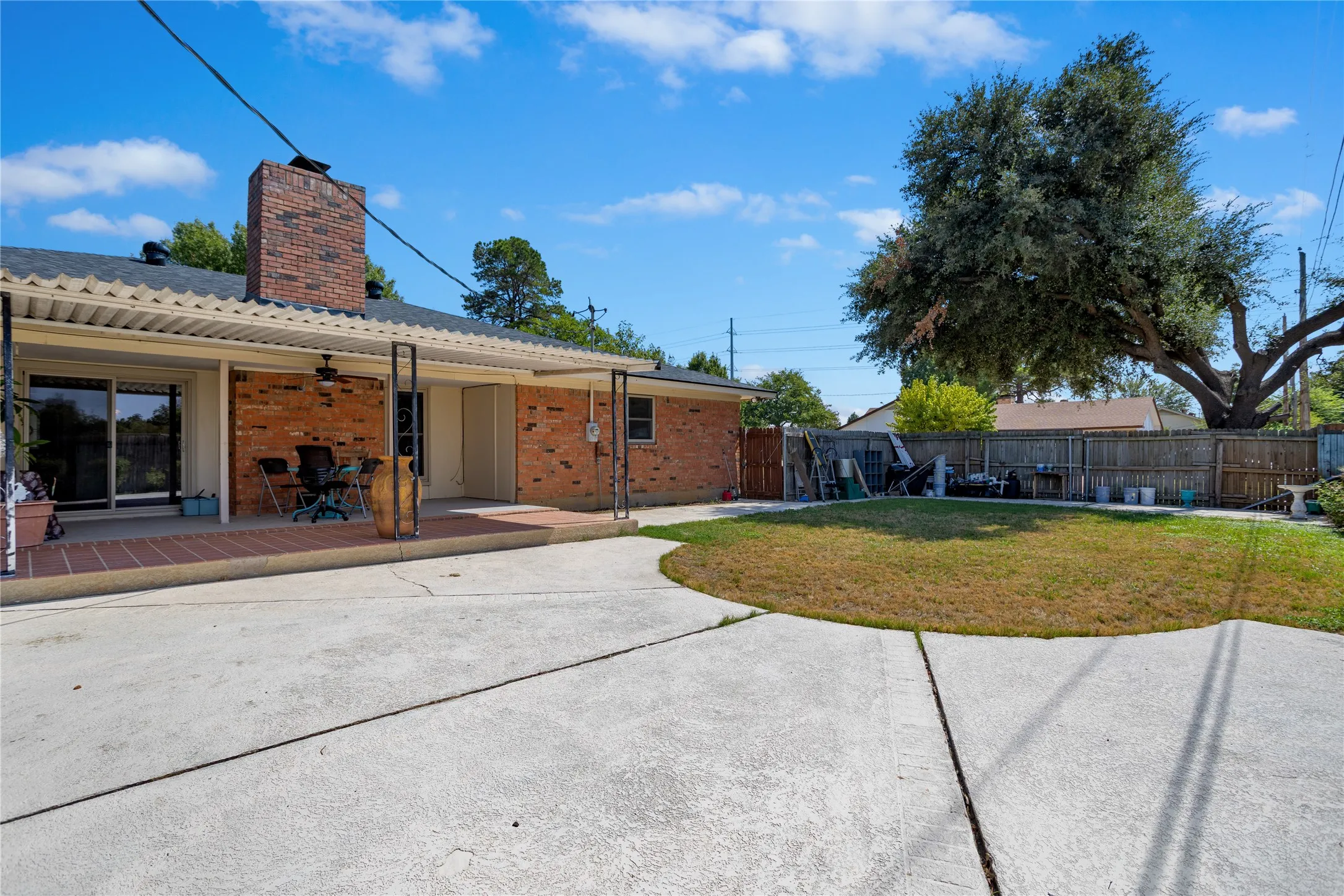 Brick exterior with a covered patio, featuring a brick chimney, sliding glass door, and an expansive concrete patio