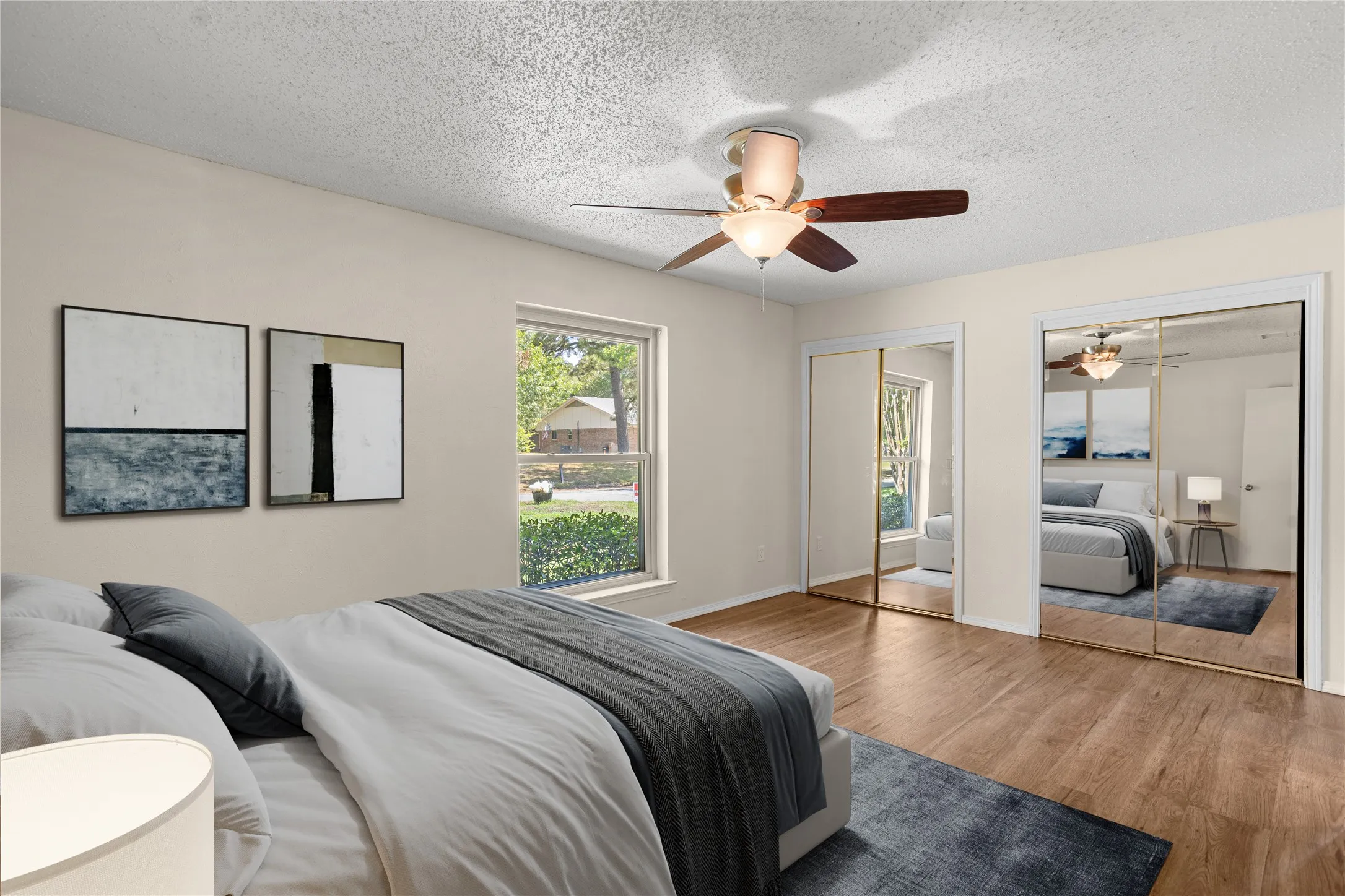 Virtually Staged Bedroom with Wood-finish flooring, ceiling fan with integrated lighting, window with exterior landscape, and mirrored closet doors