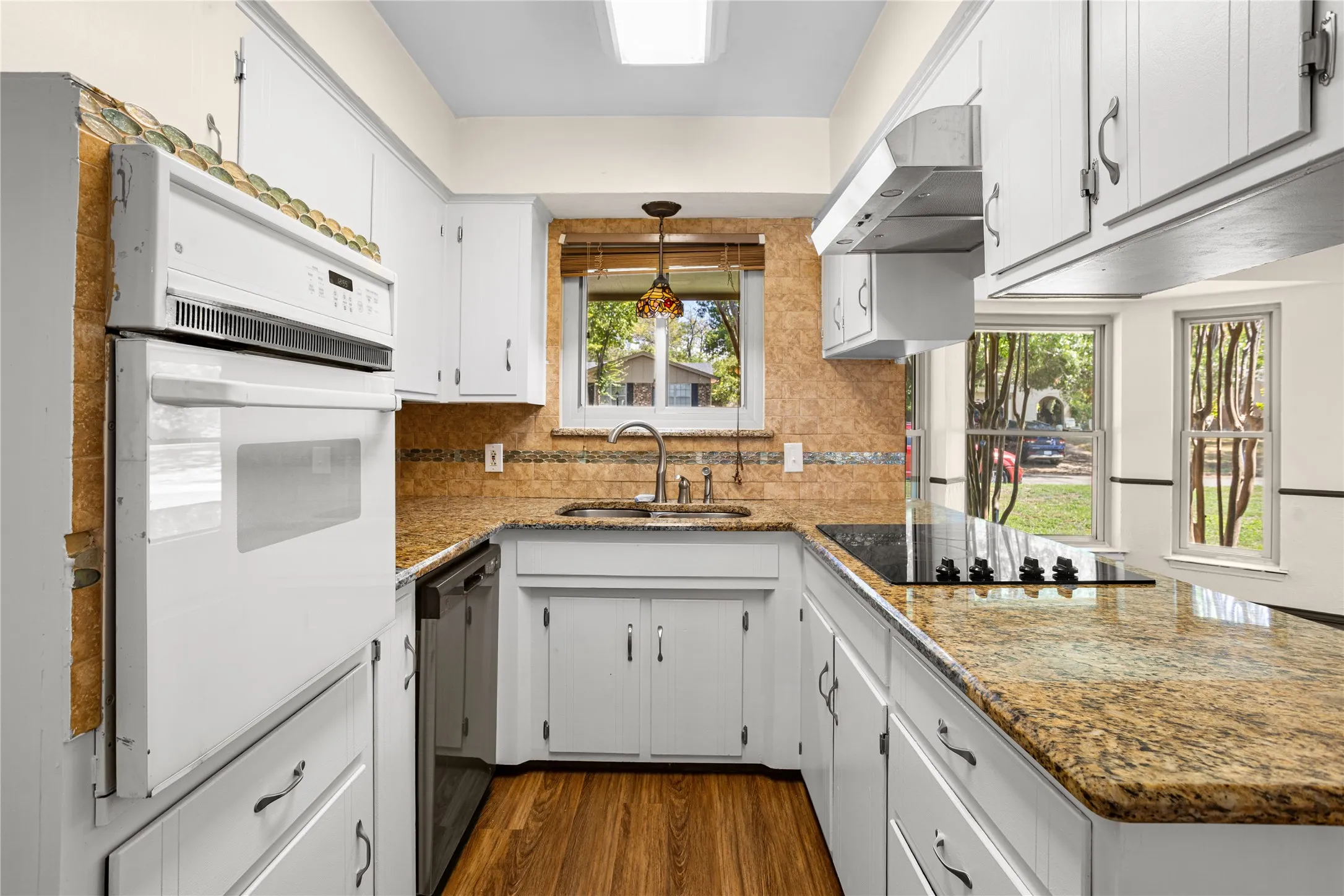 White cabinetry, stone-finish countertops, wood-finish flooring, built-in oven, and a cooktop