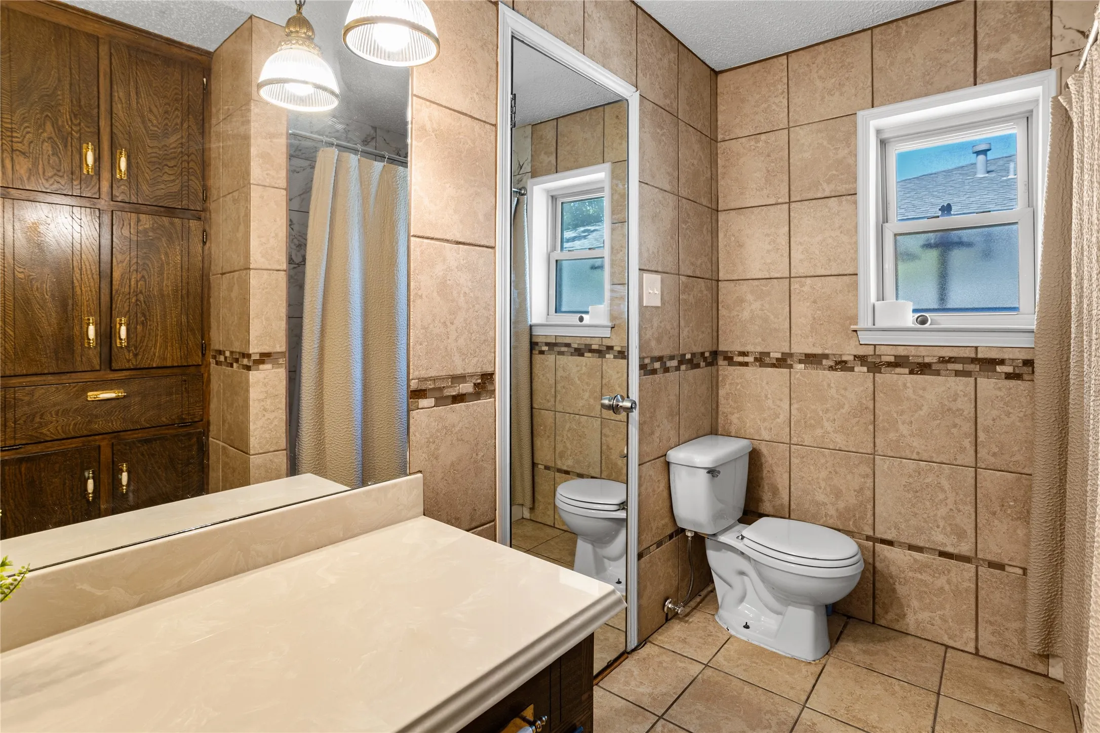 Full-height wood cabinetry, tiled walls with decorative mosaic accents, and a vanity with an integrated sink