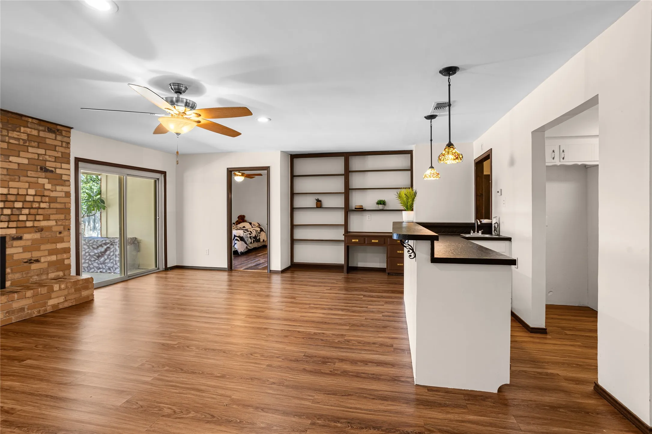 Wood-finish flooring throughout, with an exposed brick fireplace, built-in shelving, and a breakfast bar featuring pendant lighting