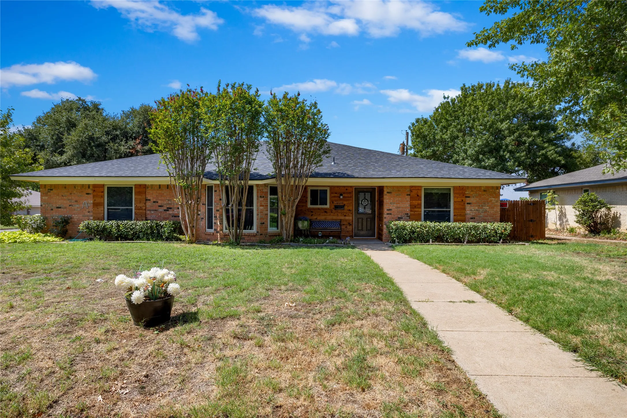 Brick exterior with a dark shingle roof, established landscaping, and a concrete pathway
