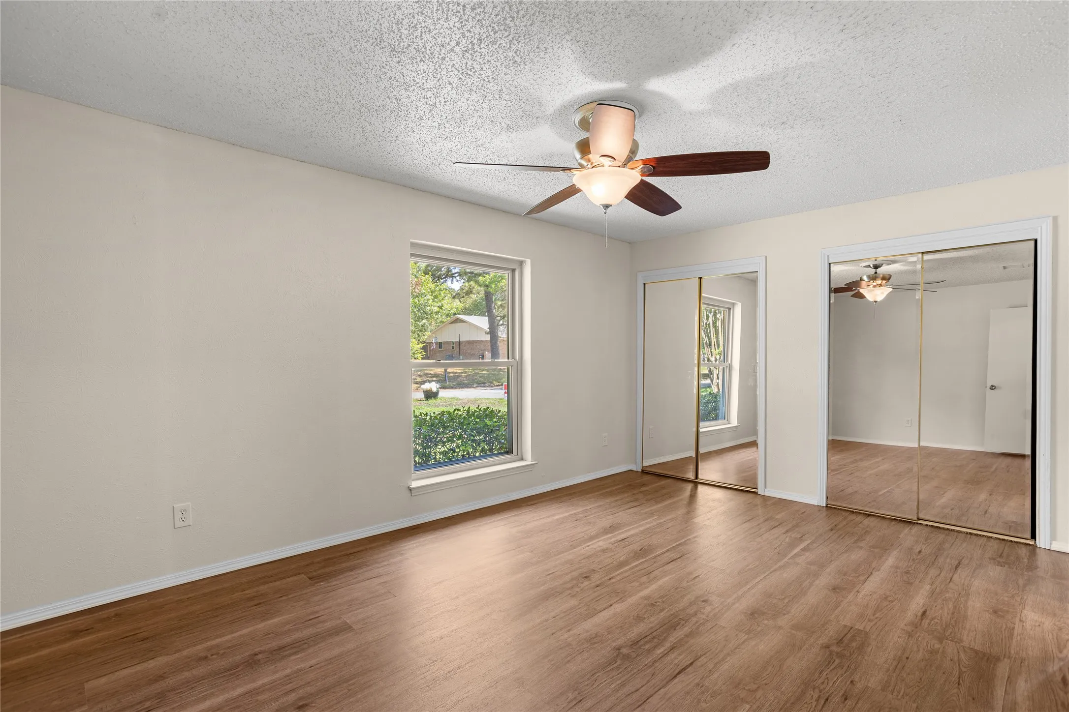 Wood-finish flooring, a window offering exterior views, a ceiling fan with integrated lighting, and mirrored sliding closet doors