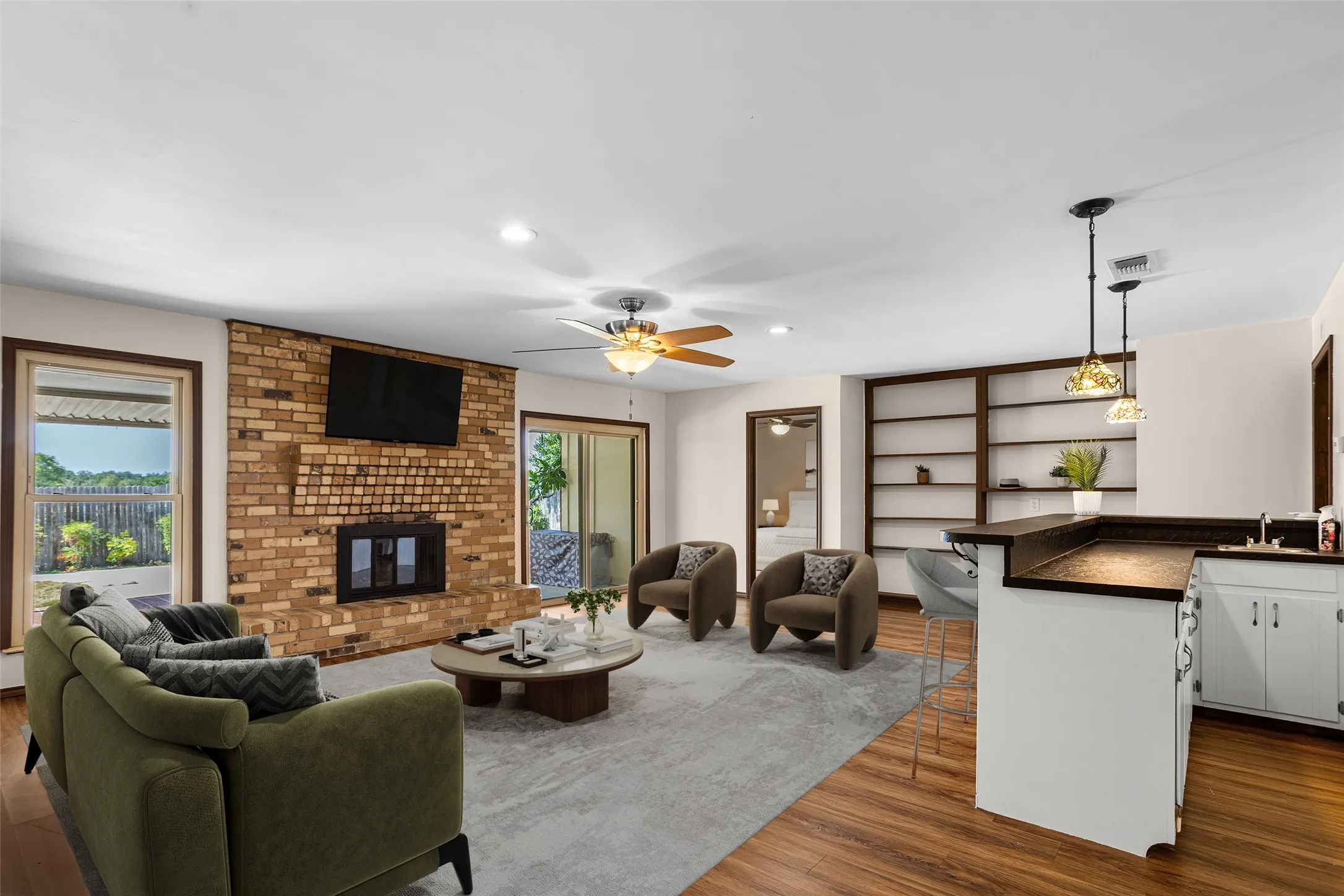Virtually Staged Living area featuring a brick fireplace, wood-finish flooring, built-in shelving, and a wet bar with pendant lighting