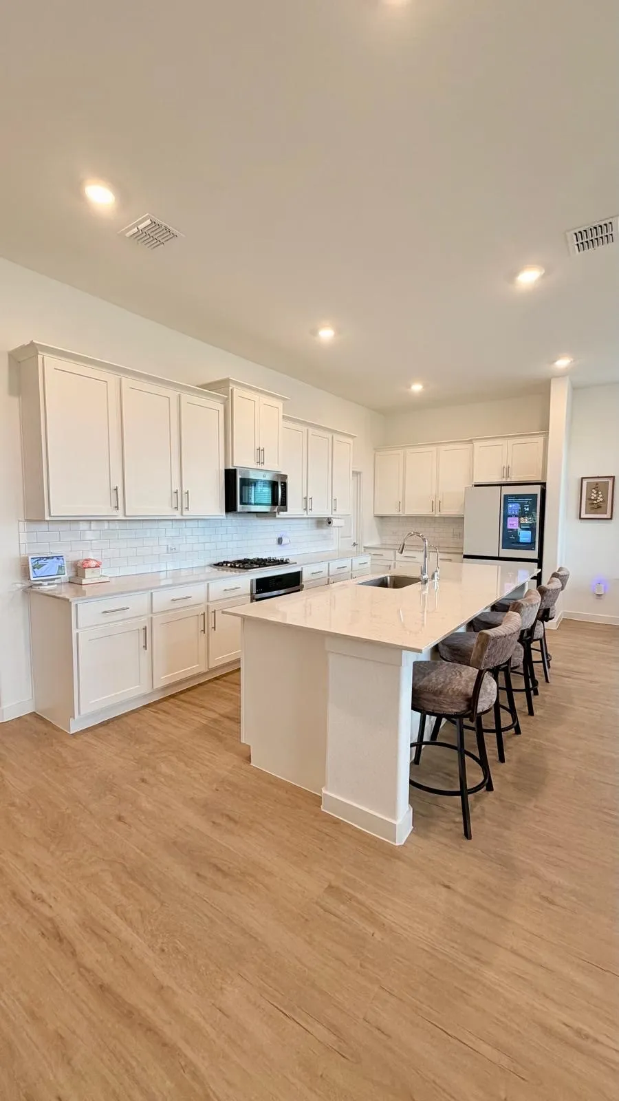 Bright kitchen featuring extensive white cabinetry, a large center island with seating, a gas range, a built-in microwave, and wood-finish flooring