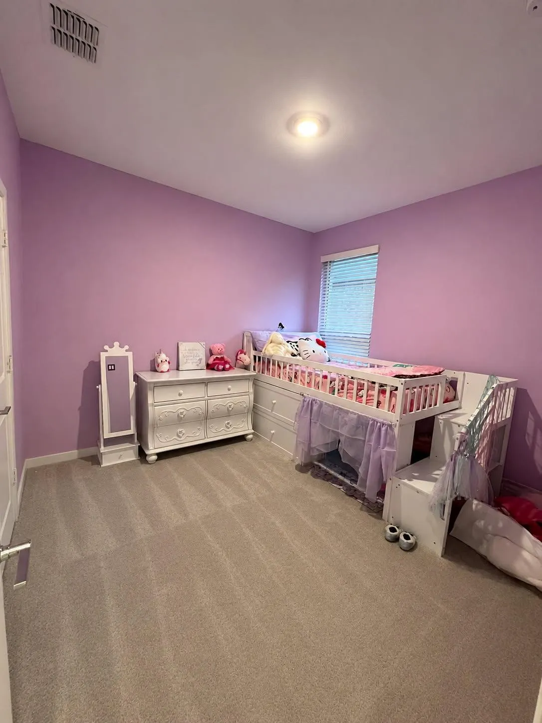 Spacious room featuring neutral carpeting, light purple walls, and a large window with blinds