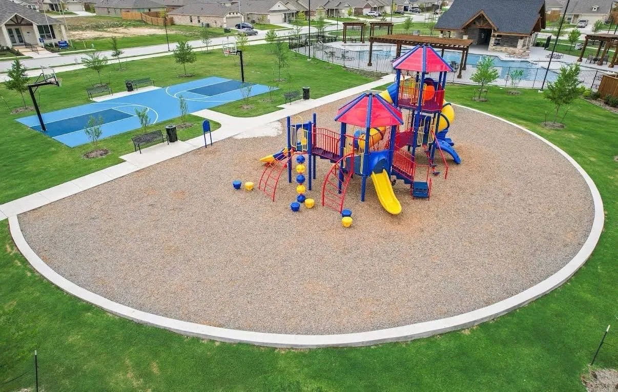 Community playground featuring multiple slides, climbing structures, and swings, set on a soft ground surface