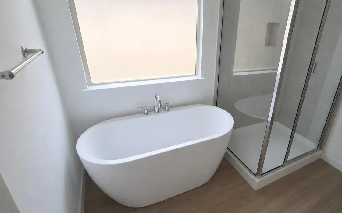 Freestanding soaking tub with chrome fixtures, accompanied by a glass-enclosed shower with a tiled interior and recessed niche