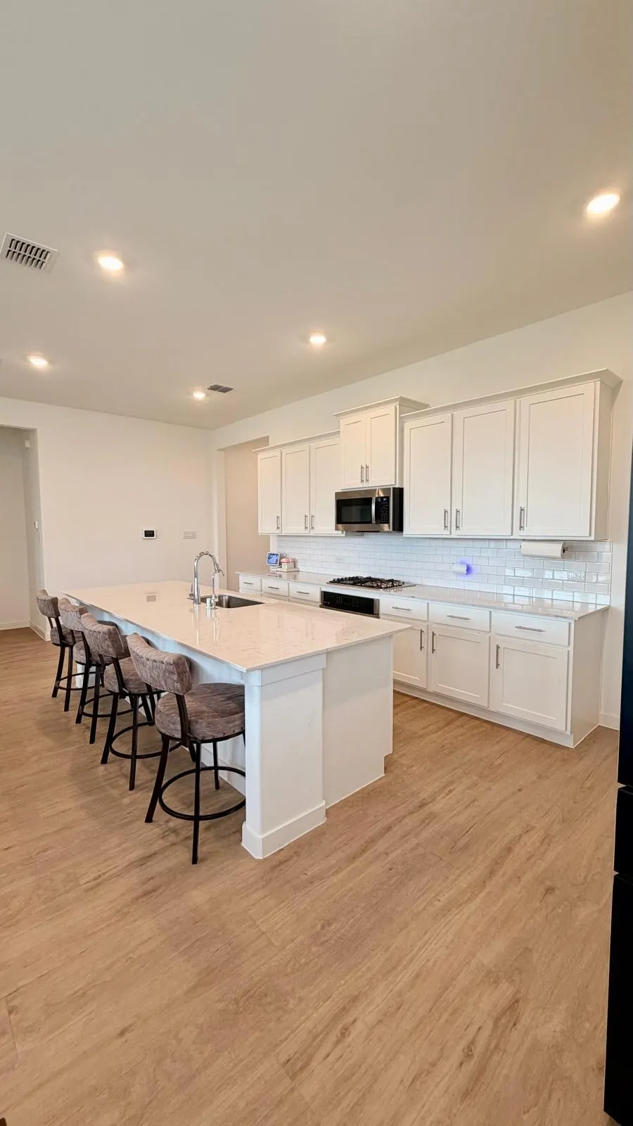 Kitchen featuring a large central island with seating, light-toned countertops, white shaker-style cabinetry, stainless steel appliances, and wood-finish flooring