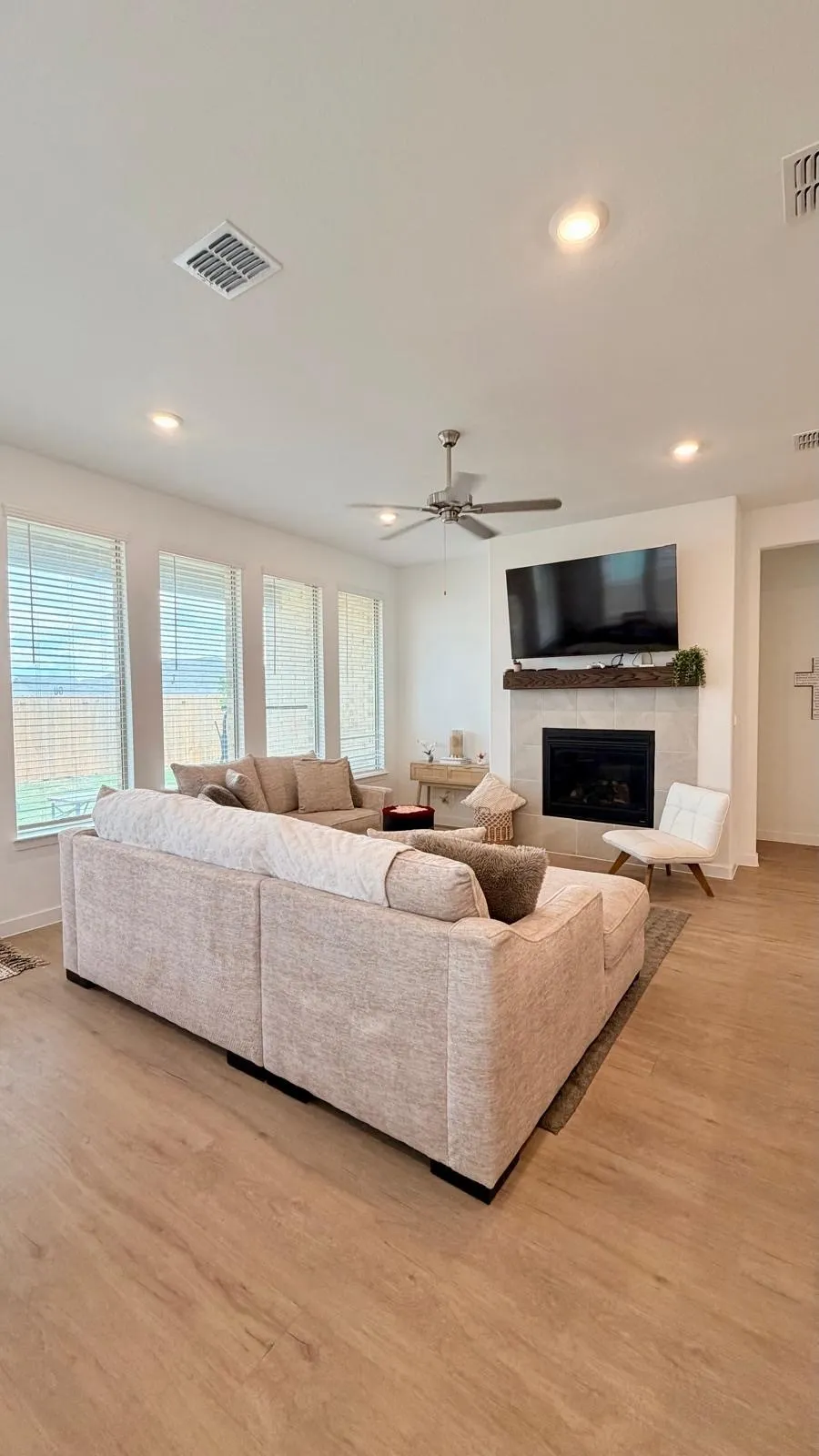 Spacious living area featuring wood-finish flooring, a fireplace with a mantel, multiple windows, recessed lighting, and a ceiling fan